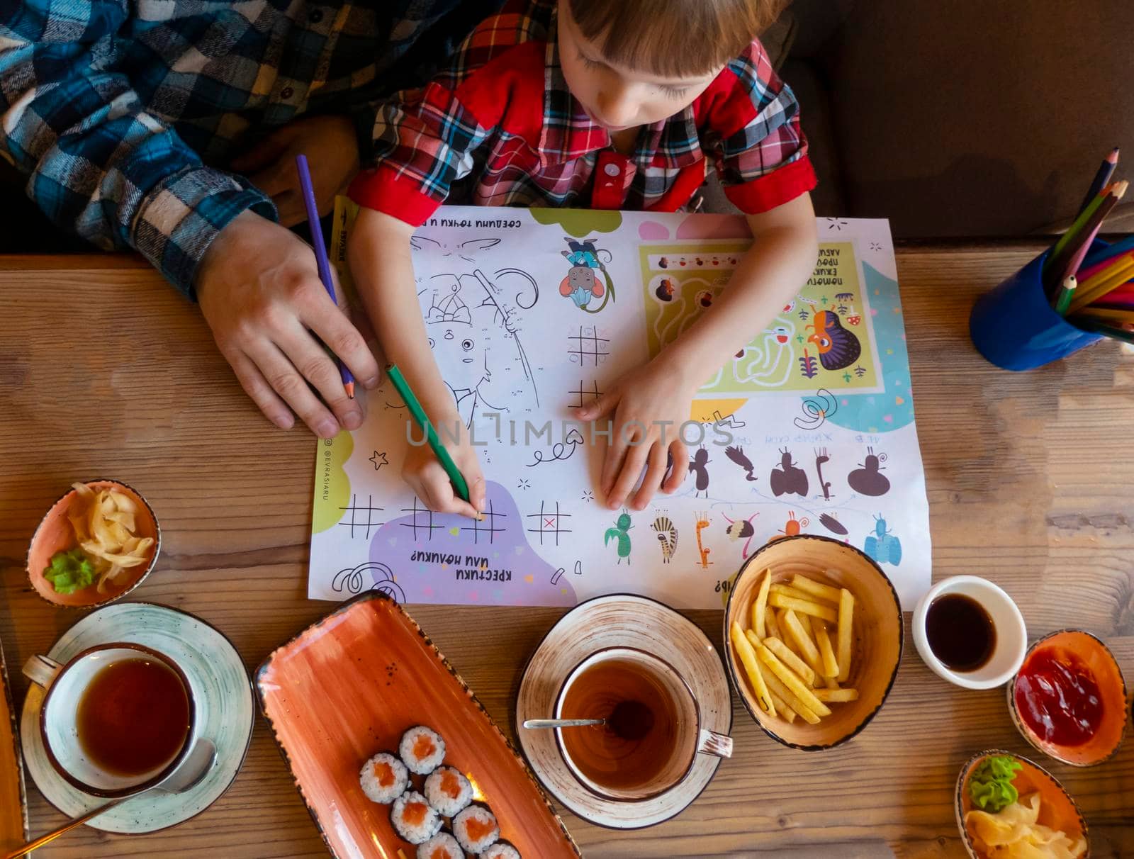 a child with his father in a restaurant draws a coloring book, waiting for cooking