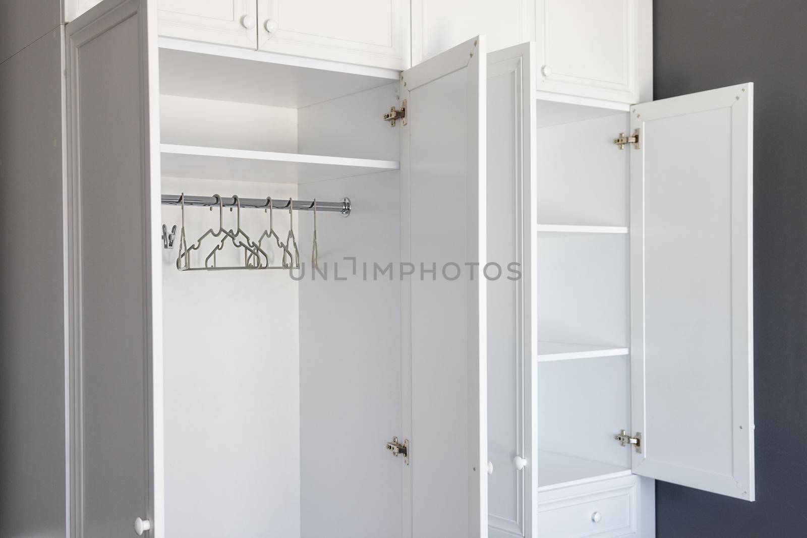 close-up, open white wardrobe with shelves and hangers for business clothes, on a dark gray background. Interior of modern room, apartment in minimalist style. The concept of organizing space