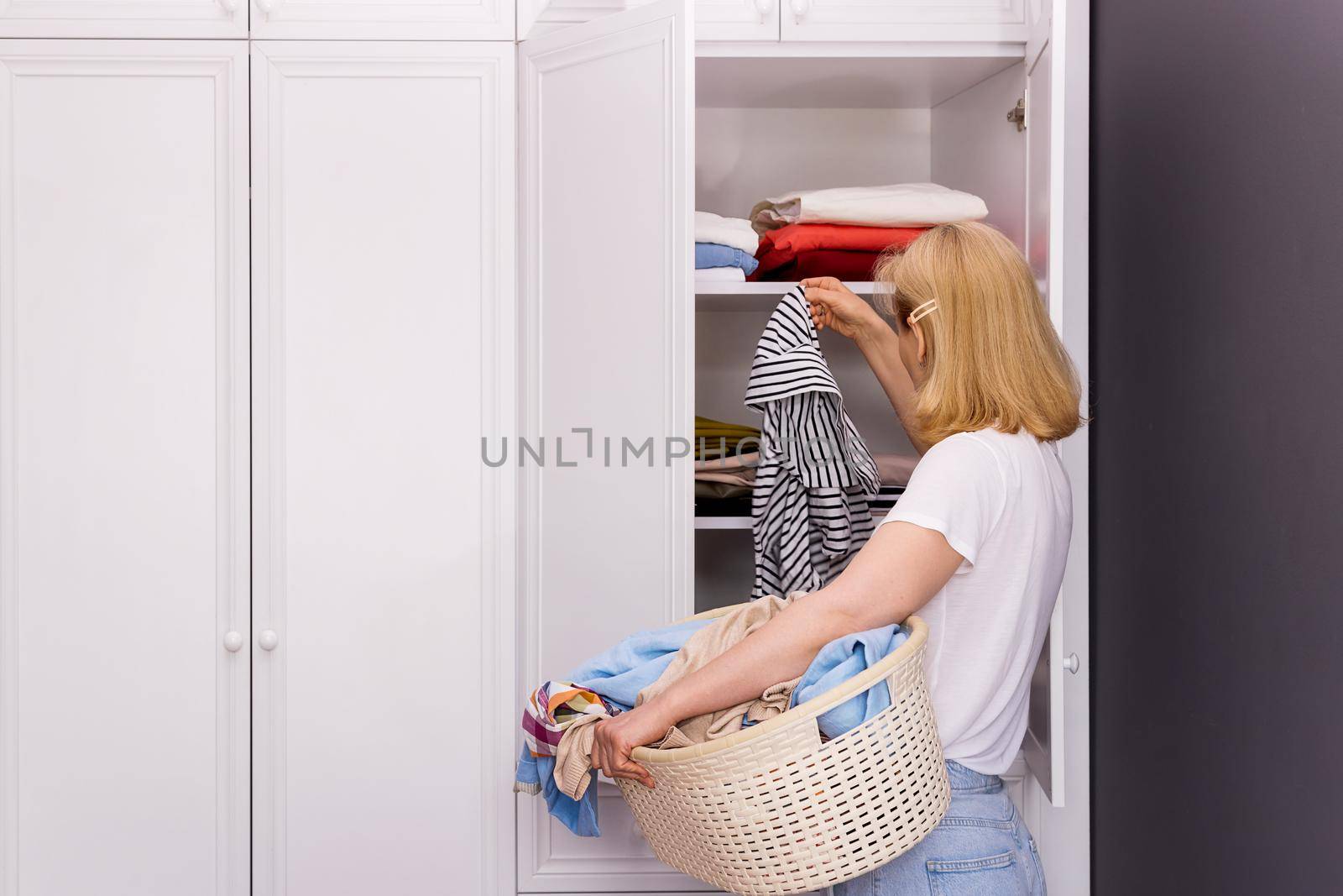 a woman stands in front of a white closet, collects things for washing by Ramanouskaya