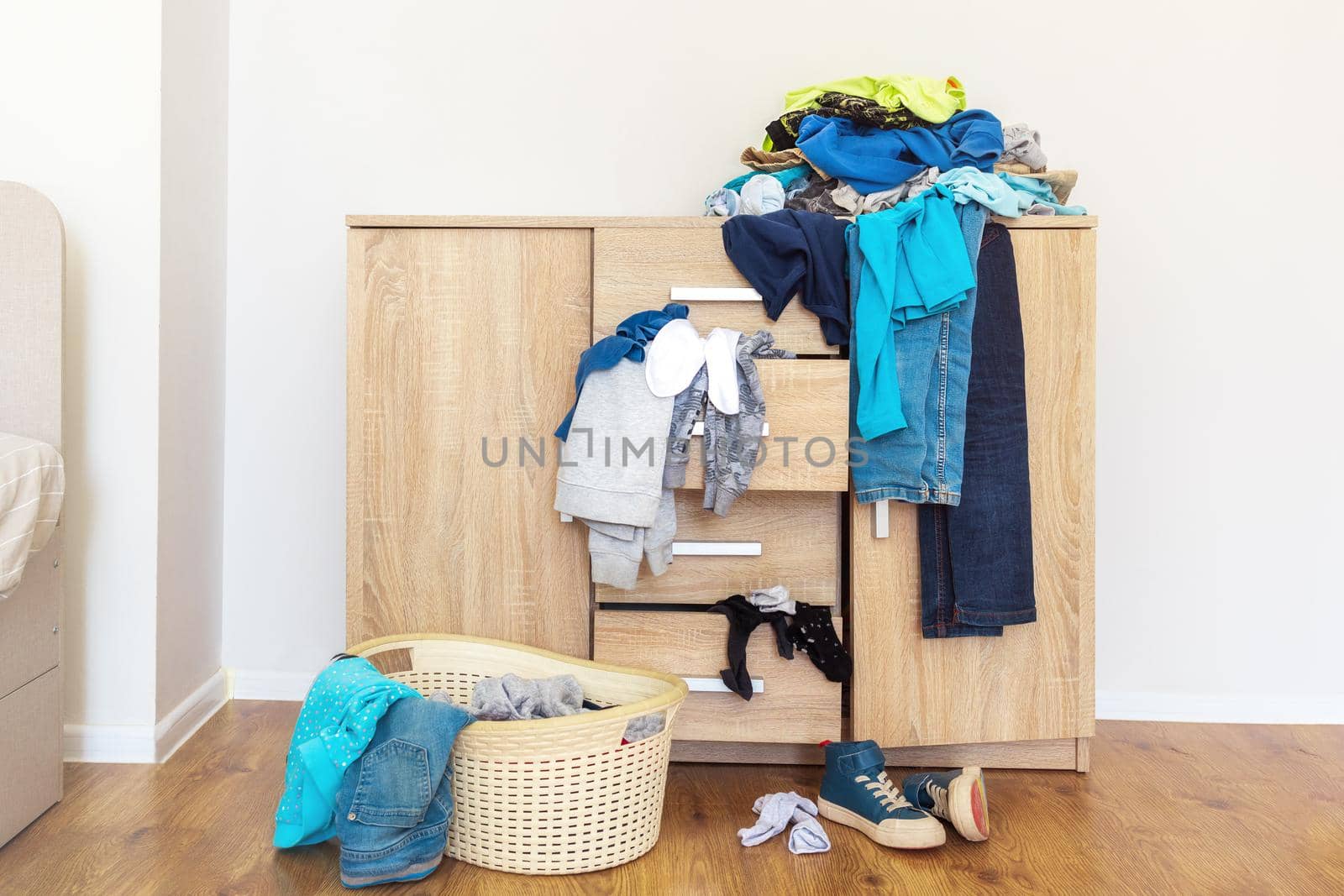 open drawers of wooden chest of drawers with clothes falling out and piles of things around in a mess. Things are laid out to send them to the laundry, wash, laundry basin. Light background copy-paste