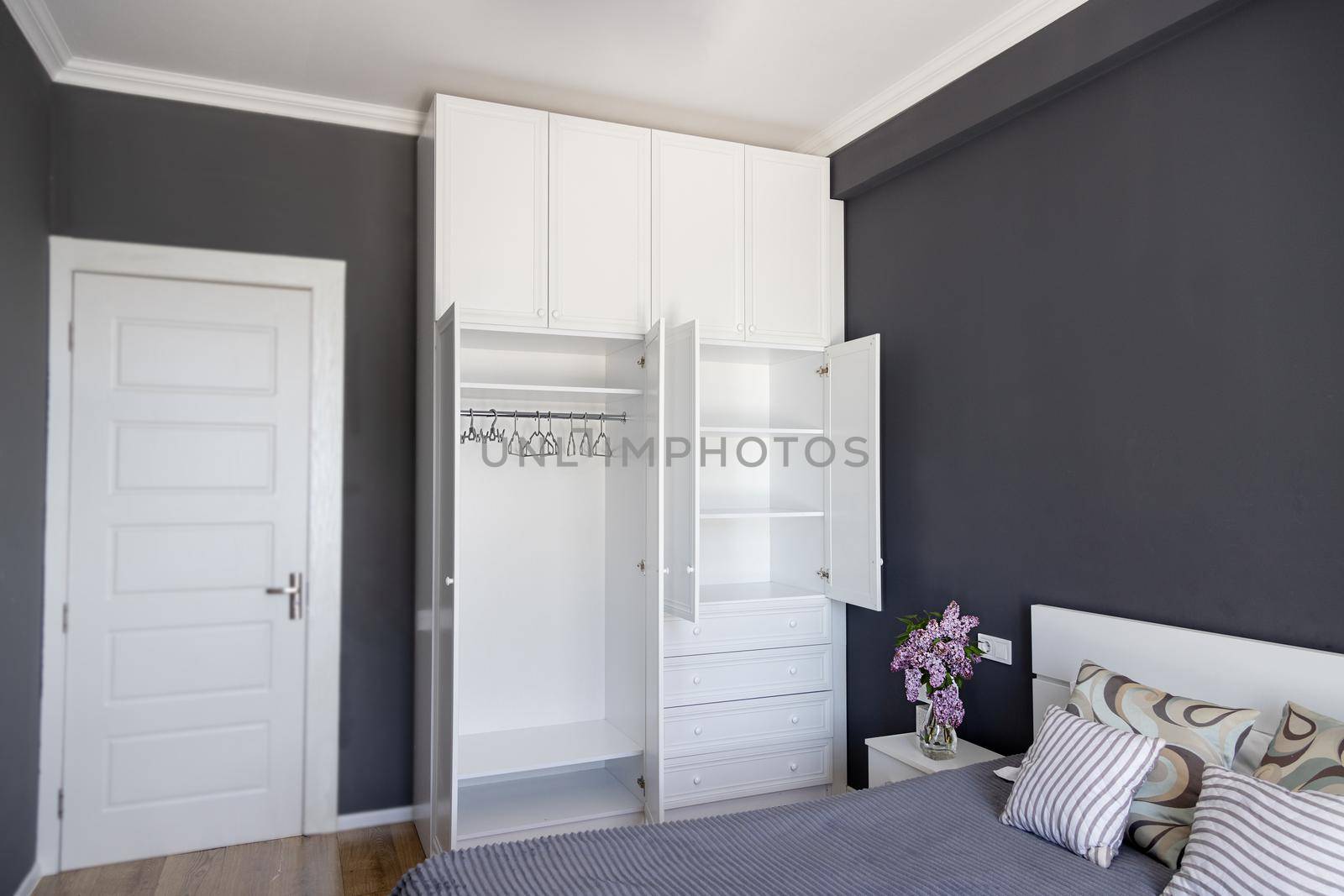 In a dark room, in the bedroom there is light furniture. Minimalistic apartments. White empty wardrobe with open doors and empty shelves. The concept of a new house, moving. Leave your accommodation