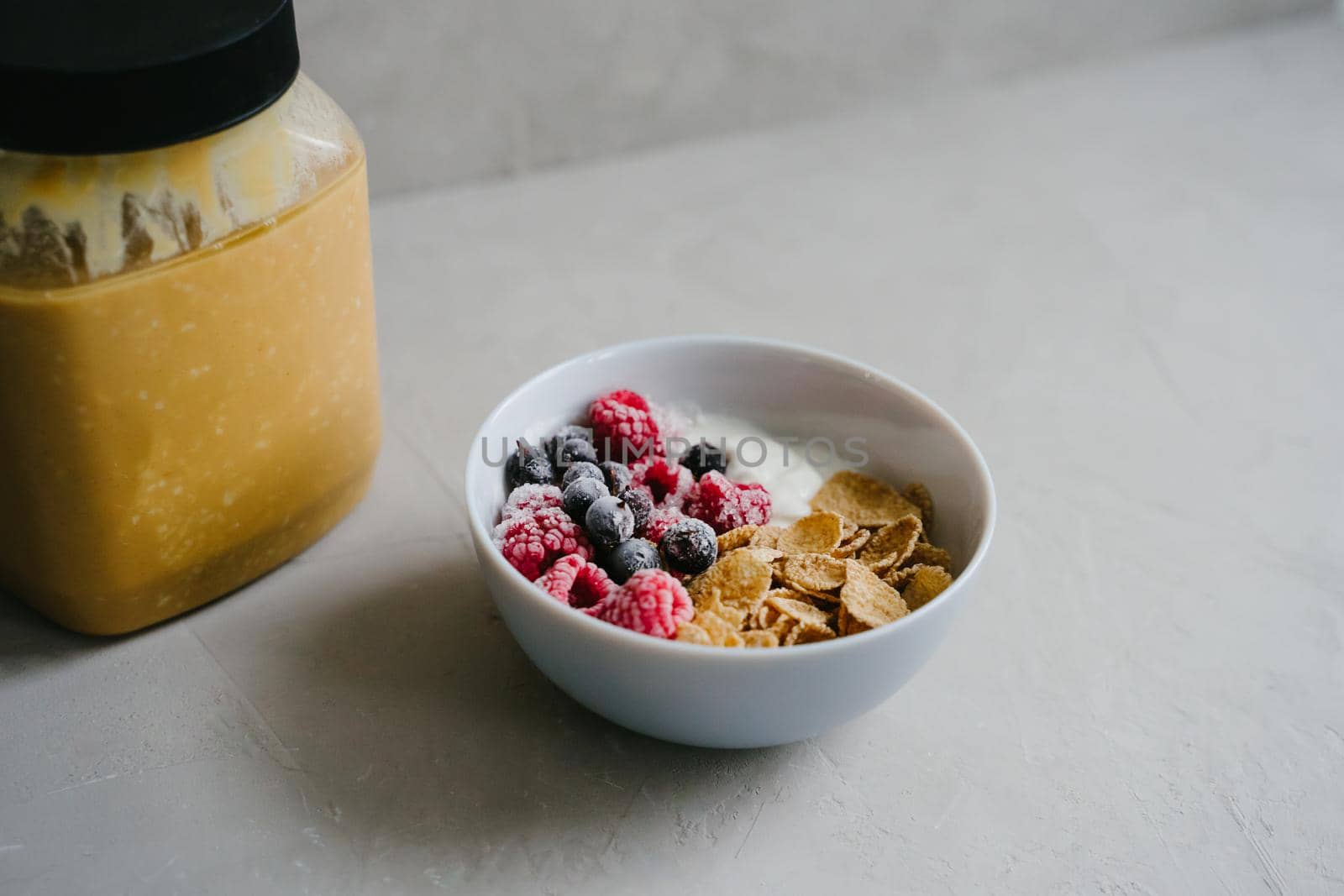 Plate with natural yogurt, cereals and berries. Delicious and healthy breakfast. Proper nutrition. Black currant and raspberry frozen. Can of peanut butter.