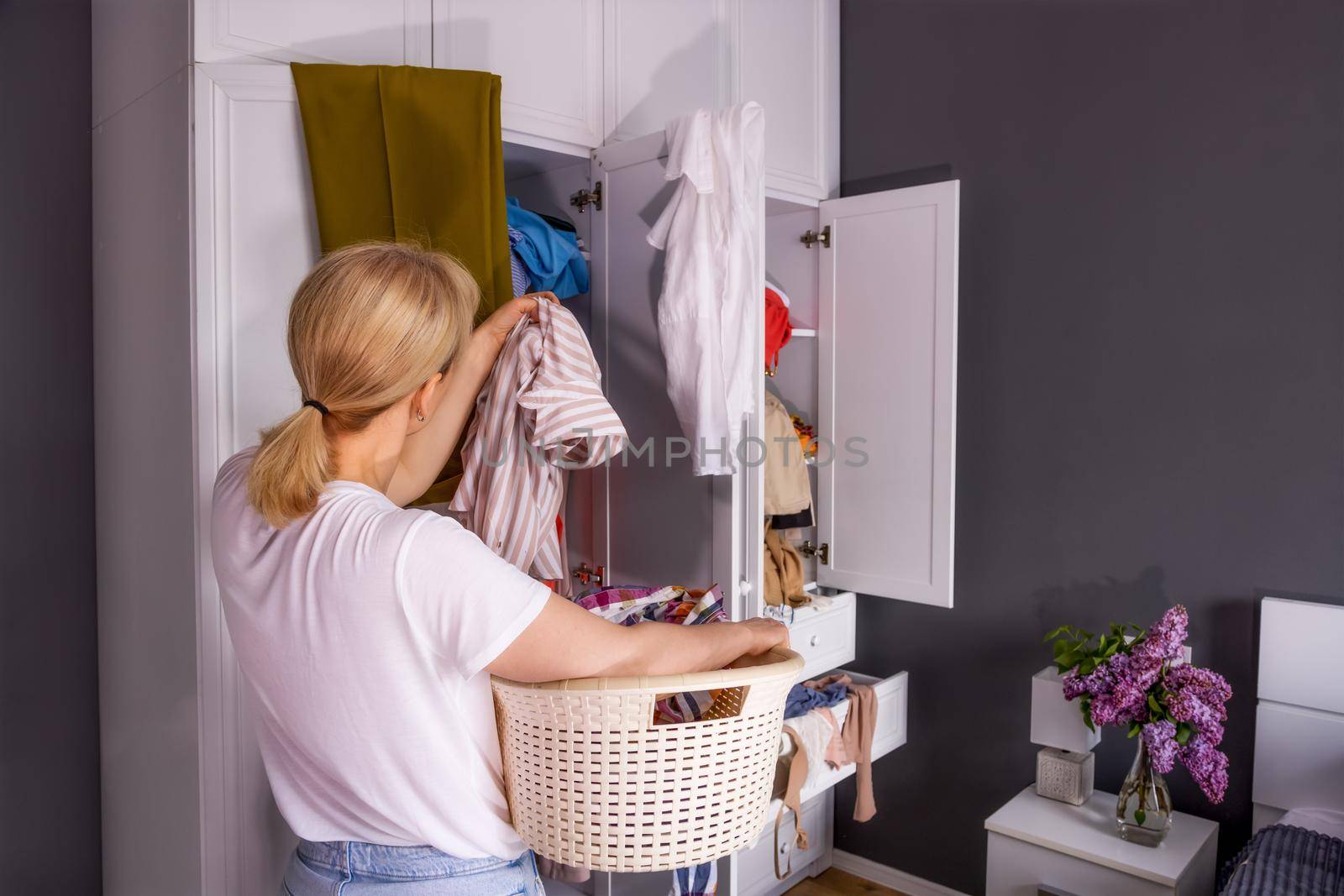 a young blonde woman stands near the wardrobe. Things are scattered in disarray. A girl collects unwanted clothes to recycle. The concept of eco-friendly consumption, space organization