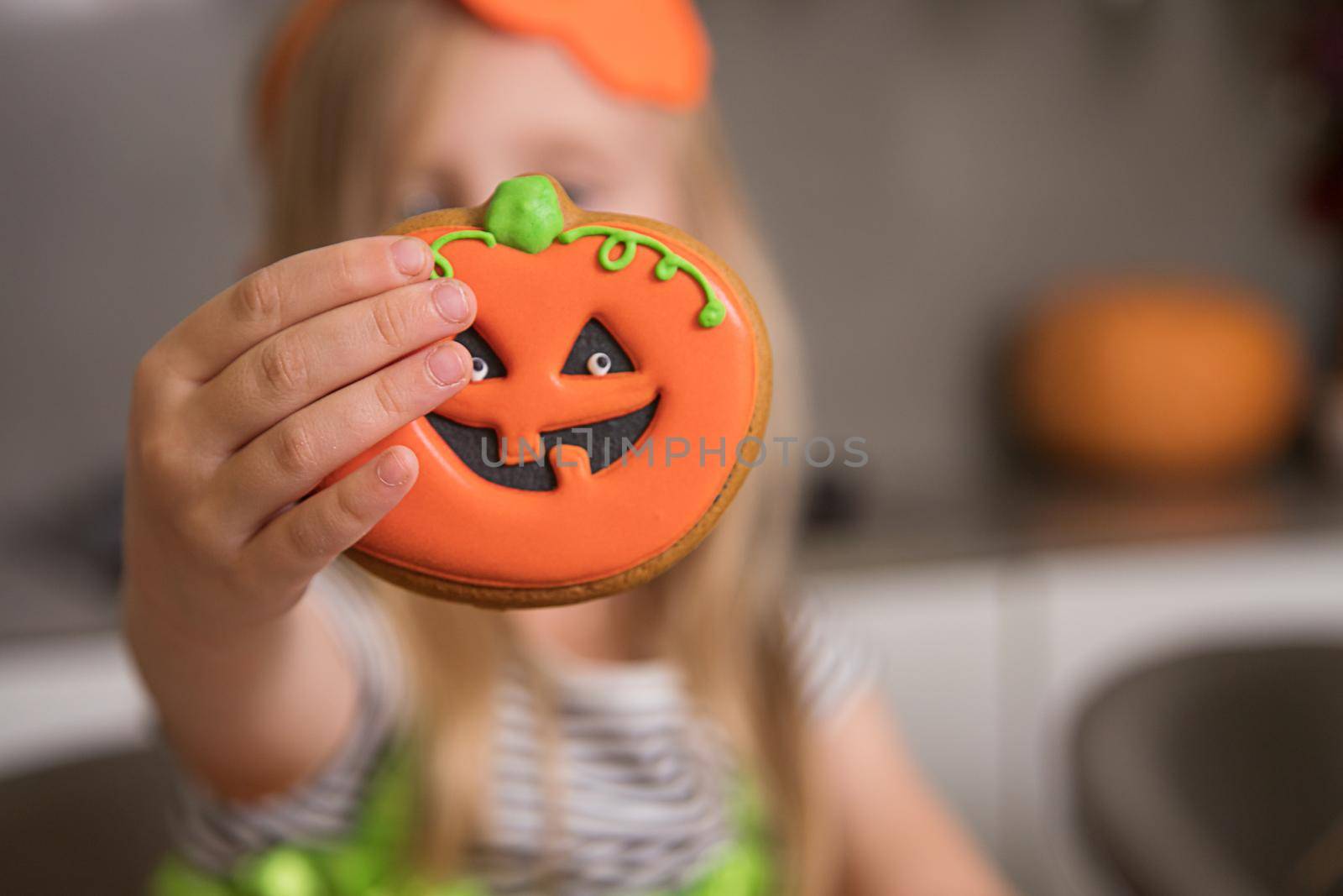 A little girl shows a gingerbread pumpkin close-up in Halloween style. by Ramanouskaya