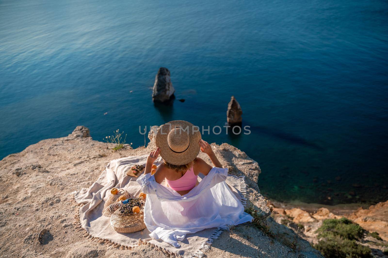 photo of a beautiful woman with long blond hair in a pink shirt and denim shorts and a hat having a picnic on a hill overlooking the sea by Matiunina