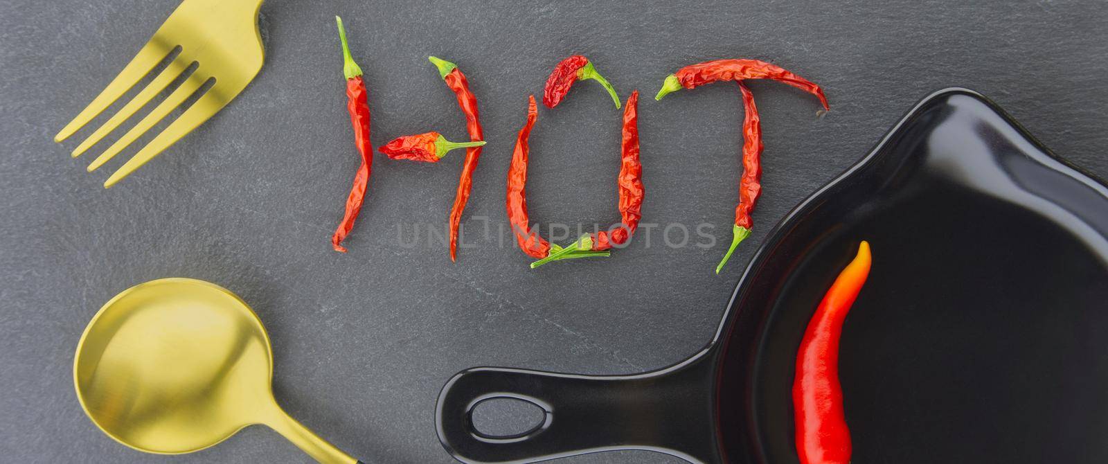 HOT spicy chili pepper still life with text formed from dried pods, gold eating utensils and a fresh chilli pepper in a skillet in a panorama banner over grey