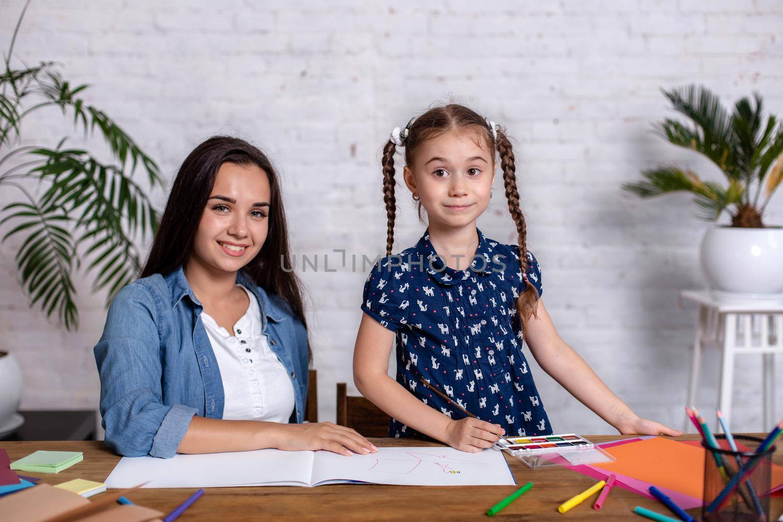 Happy family mother and daughter together draw with markers. Woman helps child girl.