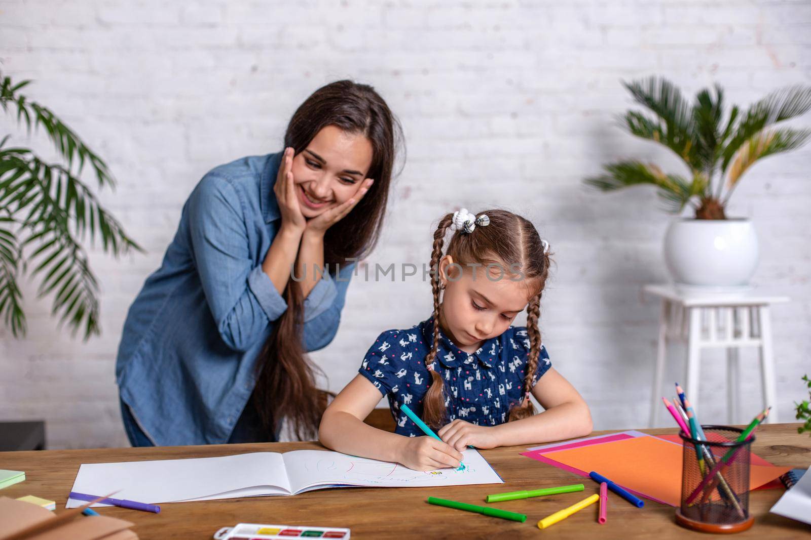 Happy family mother and daughter together draw with markers. Woman helps child girl.