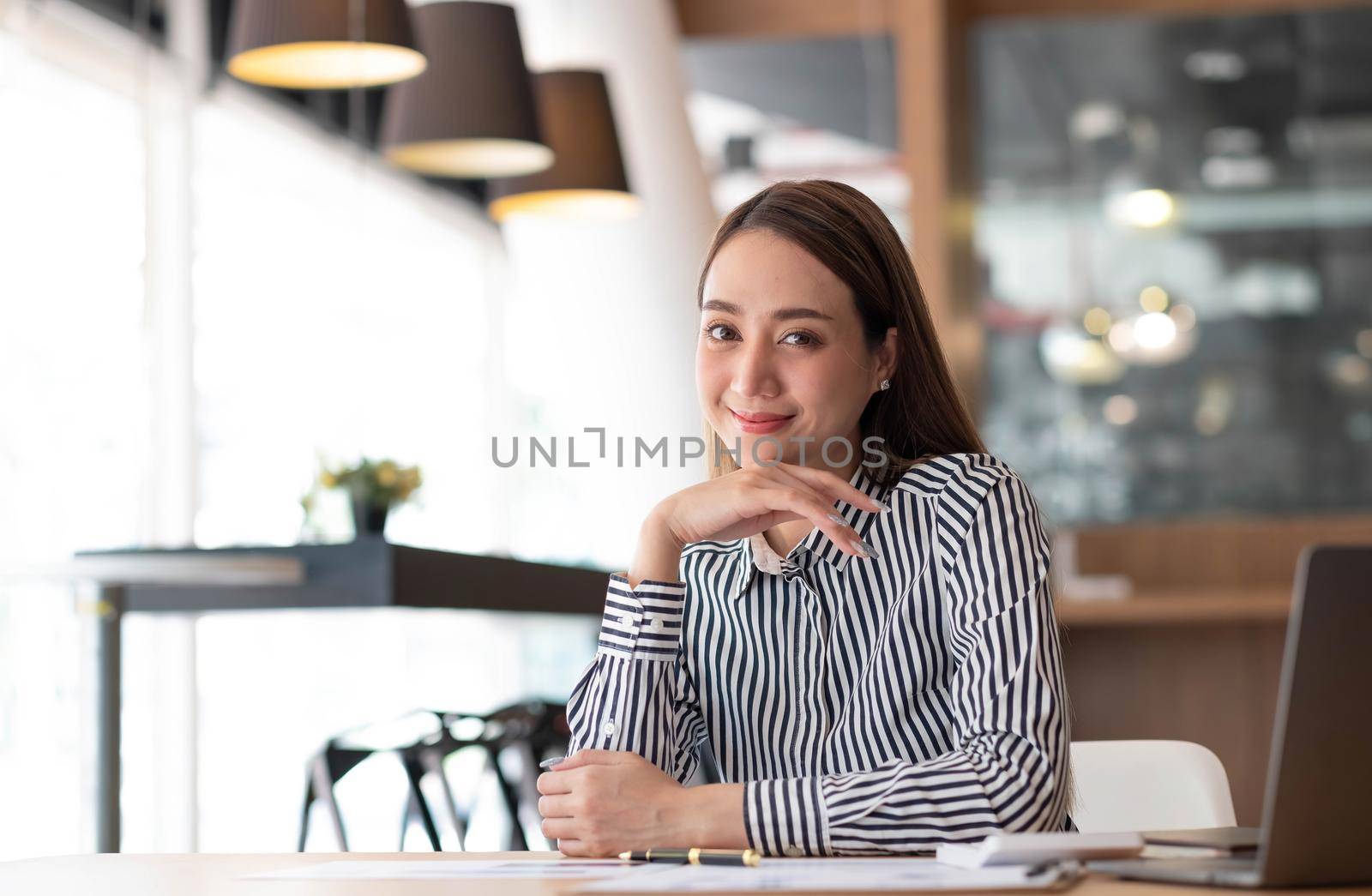 Charming Asian woman working at the office using a laptop Looking at the camera. by wichayada