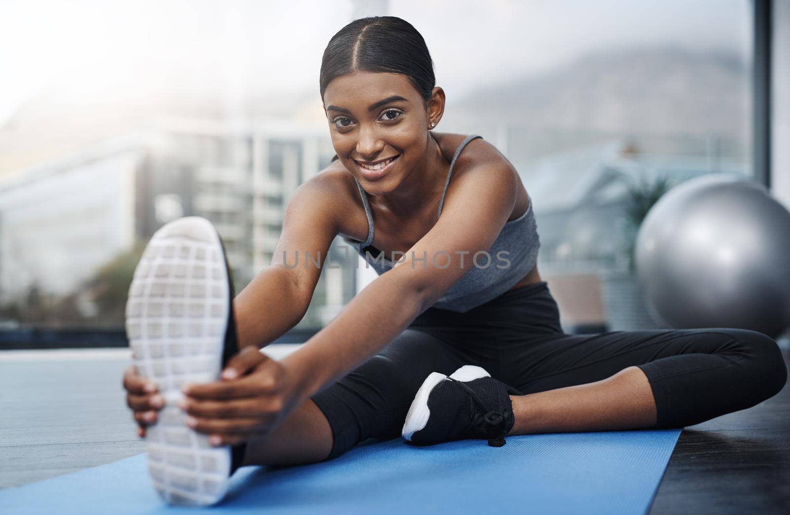Every good workout starts with a positive attitude. a beautiful young woman smiling while sitting down and doing stretching exercises on her gym mat at home