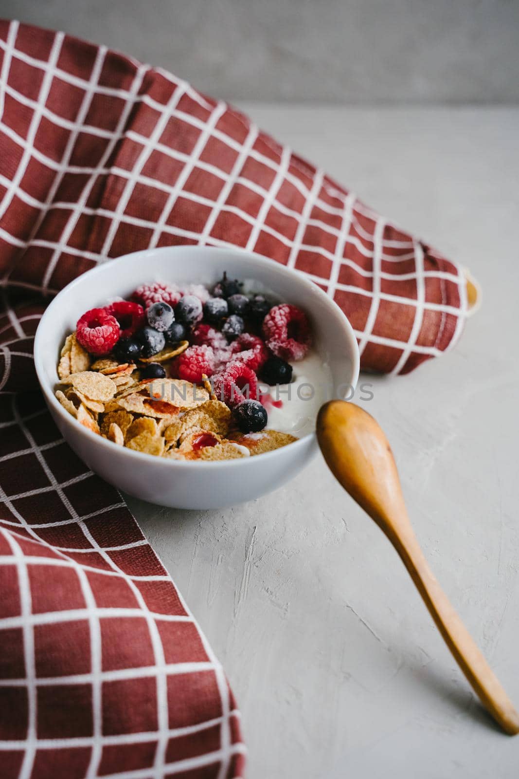 Delicious and healthy breakfast. Natural yogurt, cereals and berries. Frozen blackcurrant berries and raspberries. Wooden spoon. Multi-lacquered cereals for breakfast. Vertical photo.