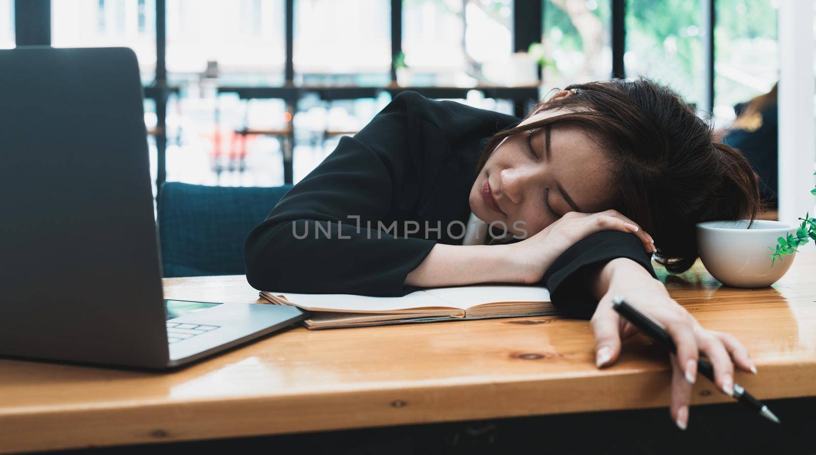 Tired or exhausted young business woman napping on working desk in front of her laptop in office.