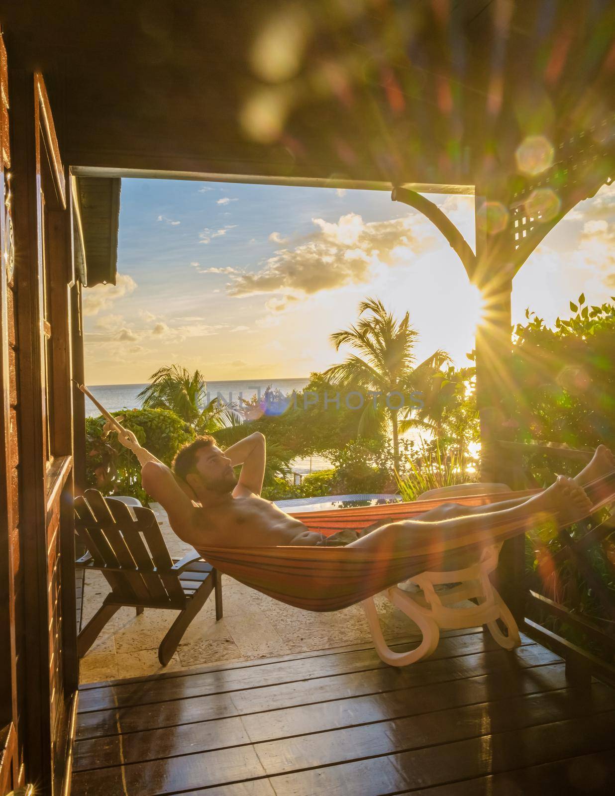 Young men in swim shorts sunbathing in a hammock at Saint Lucia Caribbean, men at infinity pool during sunset. man in swim shorts at the pool