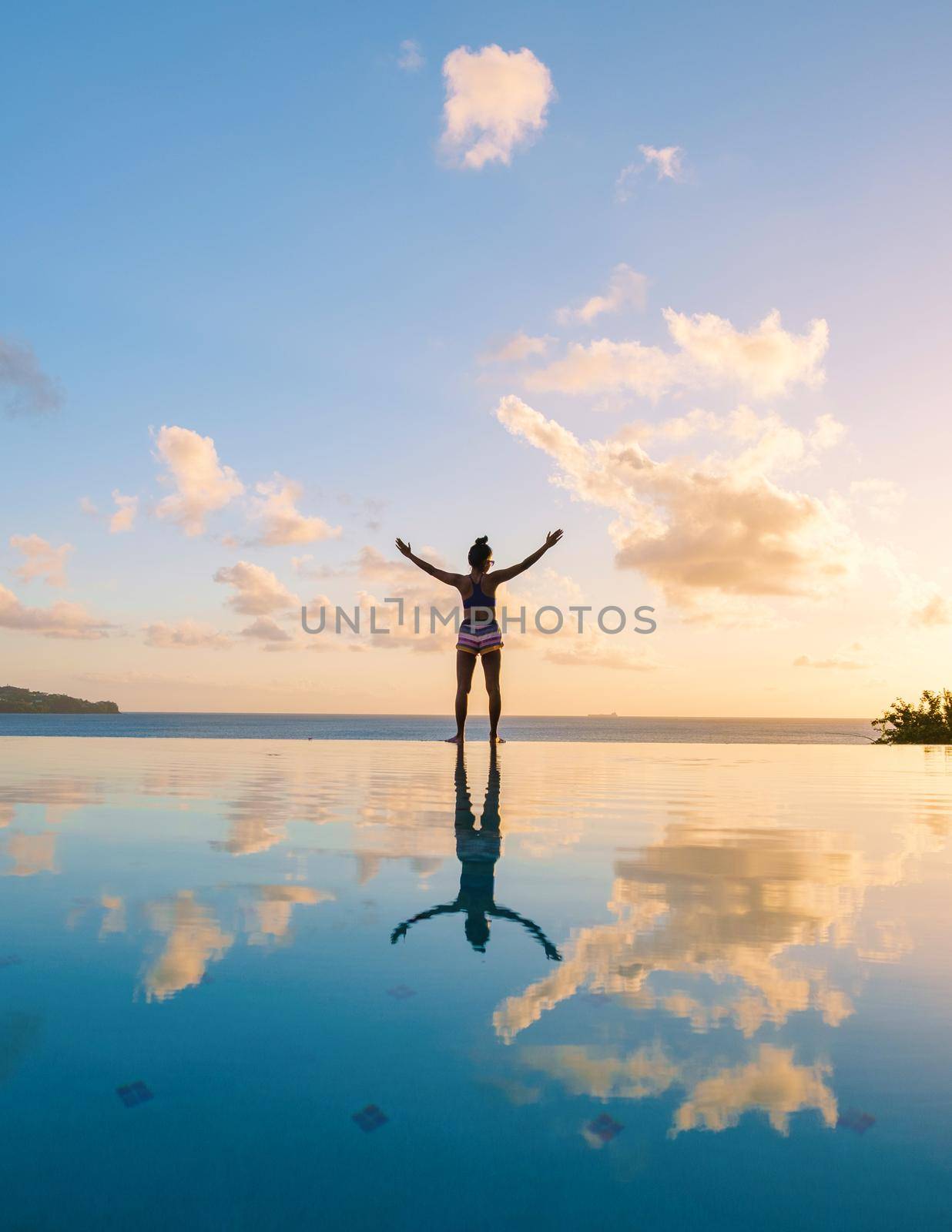Young women with hands up at Saint Lucia Caribbean, men at infinity pool during sunset. women in bikini at the pool