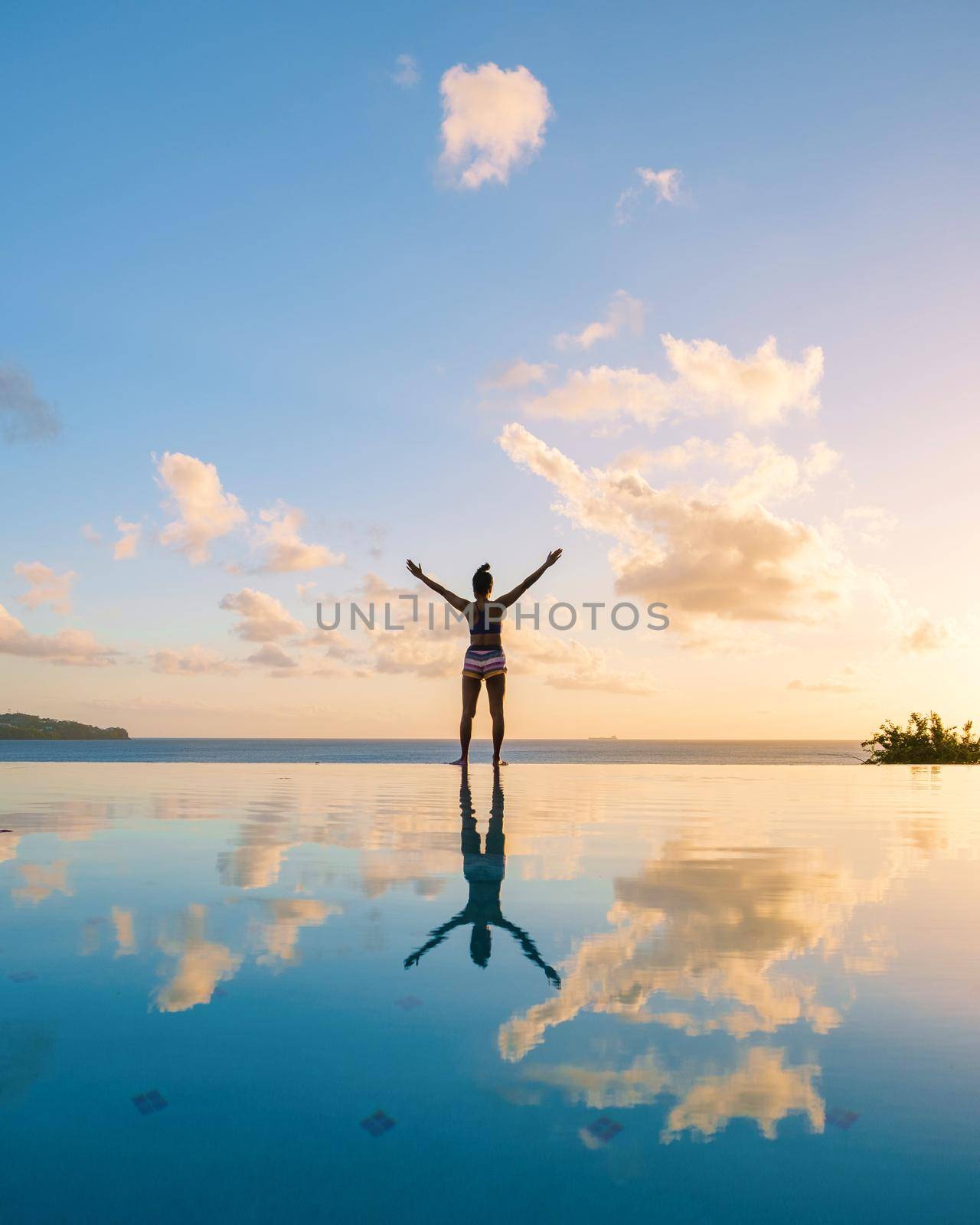 Young women with hands up at Saint Lucia Caribbean, men at infinity pool during sunset. women in bikini at the pool