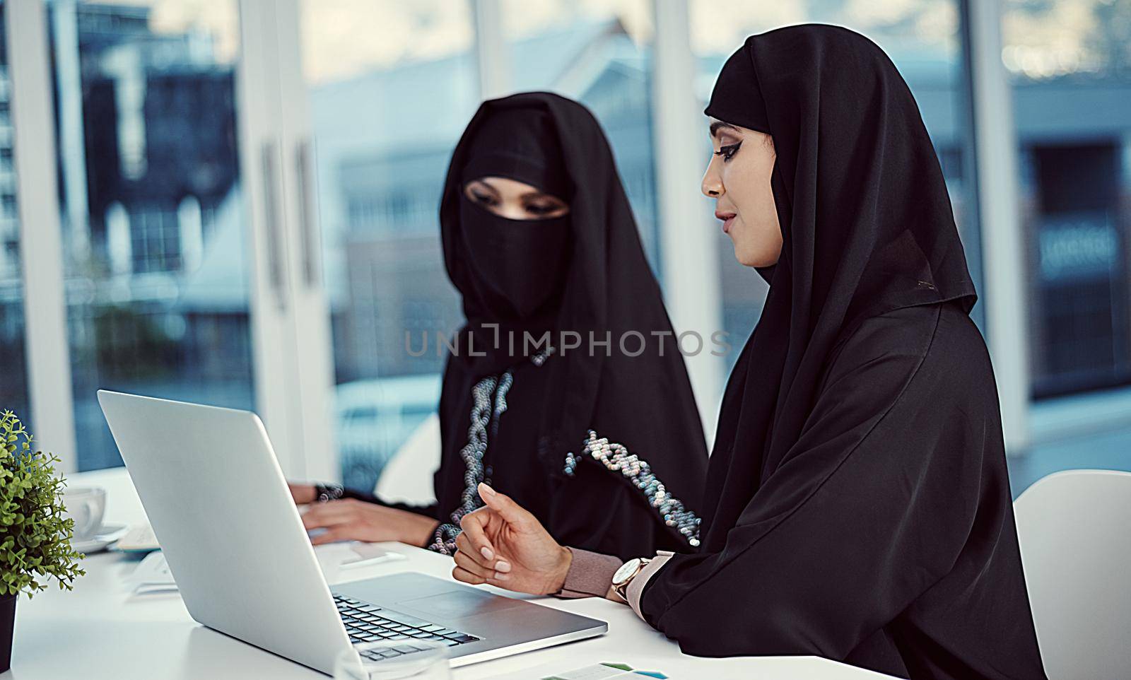 Communication and teamwork go hand in hand. two young arabic businesswomen working on a laptop in their office. by YuriArcurs