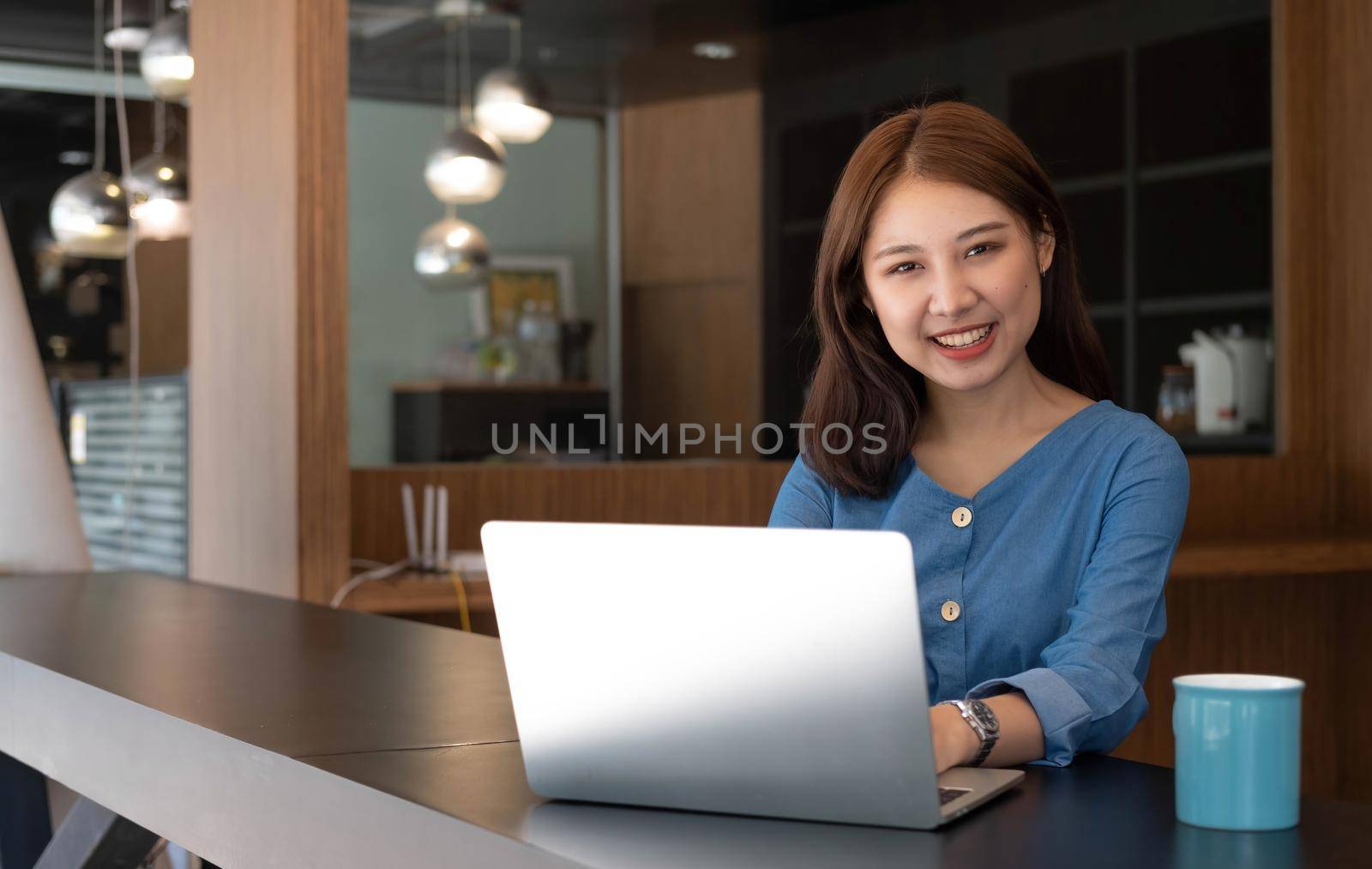 Charming Asian businesswoman working with a laptop at the office. Looking at camera..