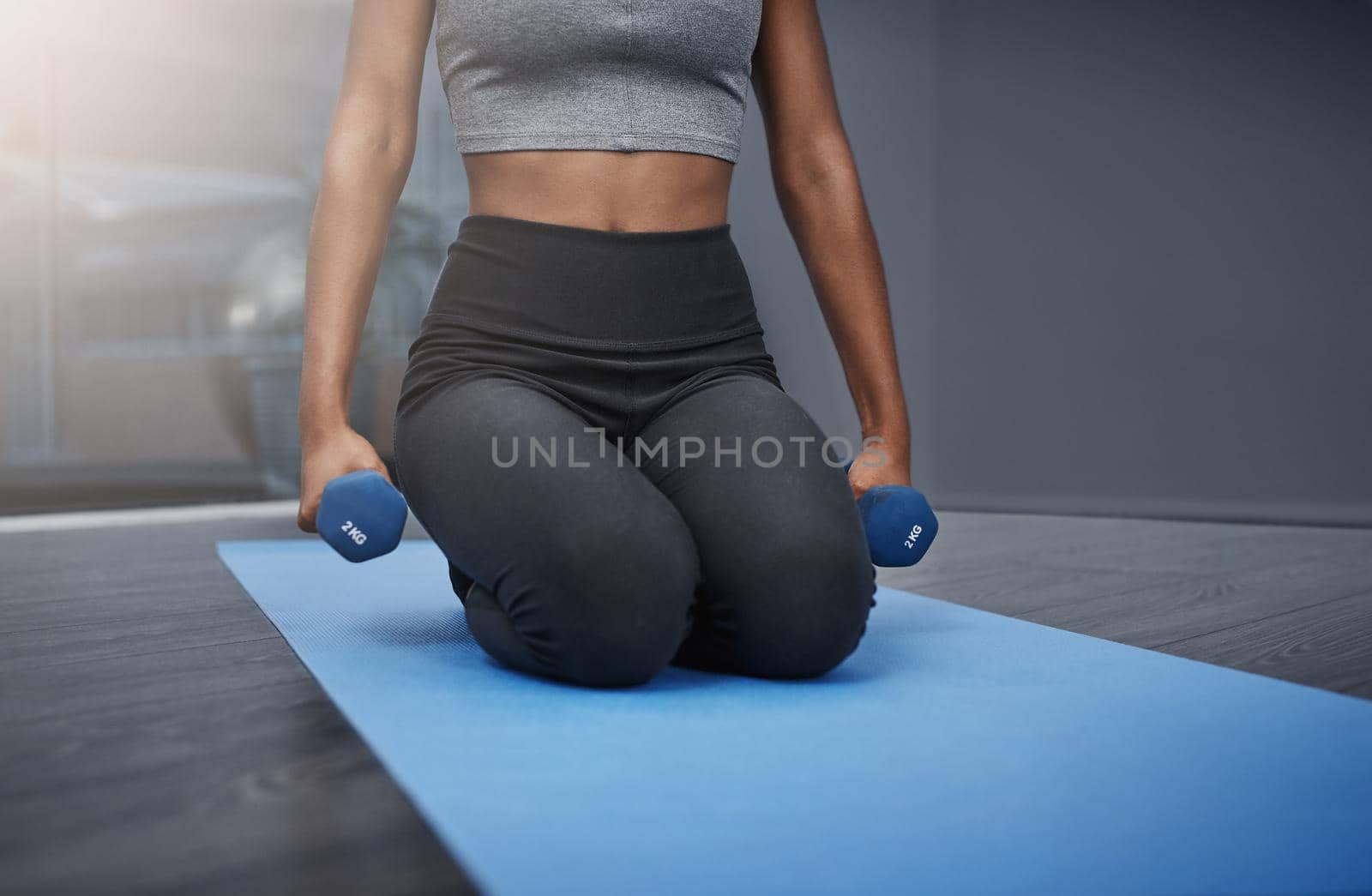 The end goal is worth every sacrifice. an unrecognizable young woman on her knees holding dumbbells while exercising on her gym mat at home. by YuriArcurs