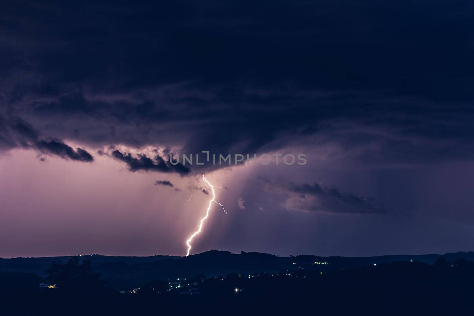 Night landscape on a background of thunderstorms. Rural silhouette and clouds with lightning flashes