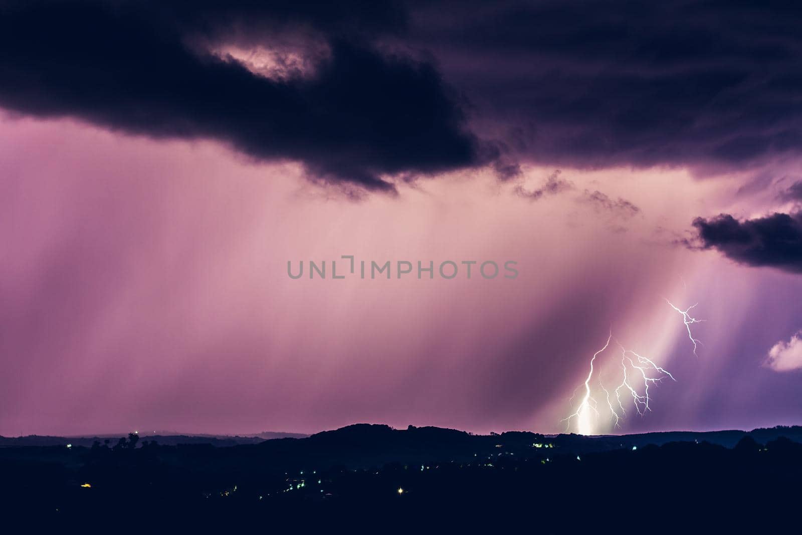 Night landscape on a background of thunderstorms. Rural silhouette and clouds with lightning flashes