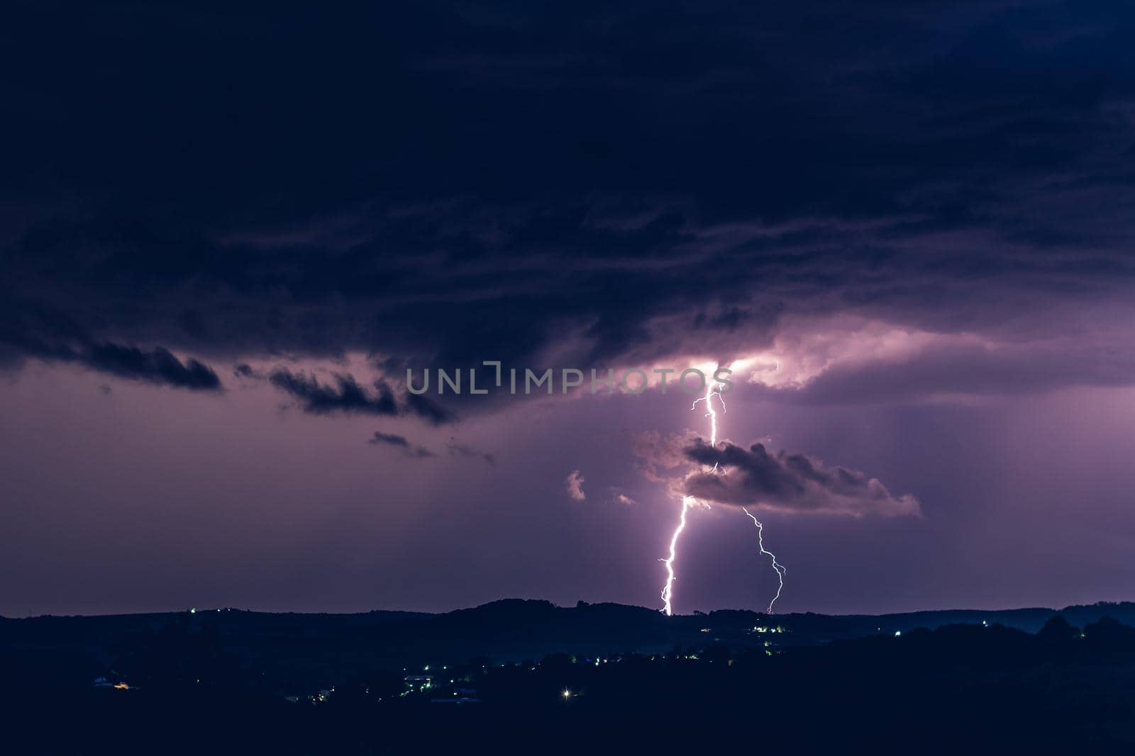 Night landscape on a background of thunderstorms. Rural silhouette and clouds with lightning flashes