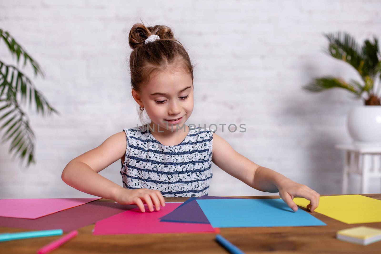 Cute little girl at the table with the colored paper