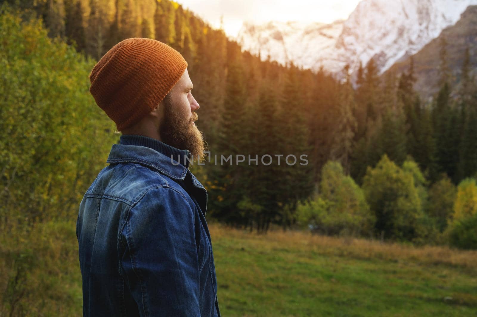 A bearded man stand on a log alone in the mountains. Healthy lifestyle concept, sunny mountain landscape.