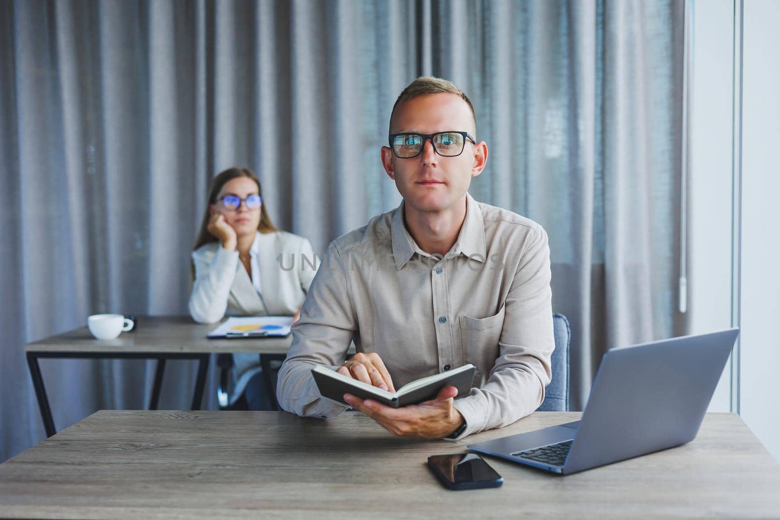 Portrait of a cheerful man, IT professional, working with a modern laptop, sitting at a table and smiling at the camera during a break, a happy human programmer in vision correction glasses
