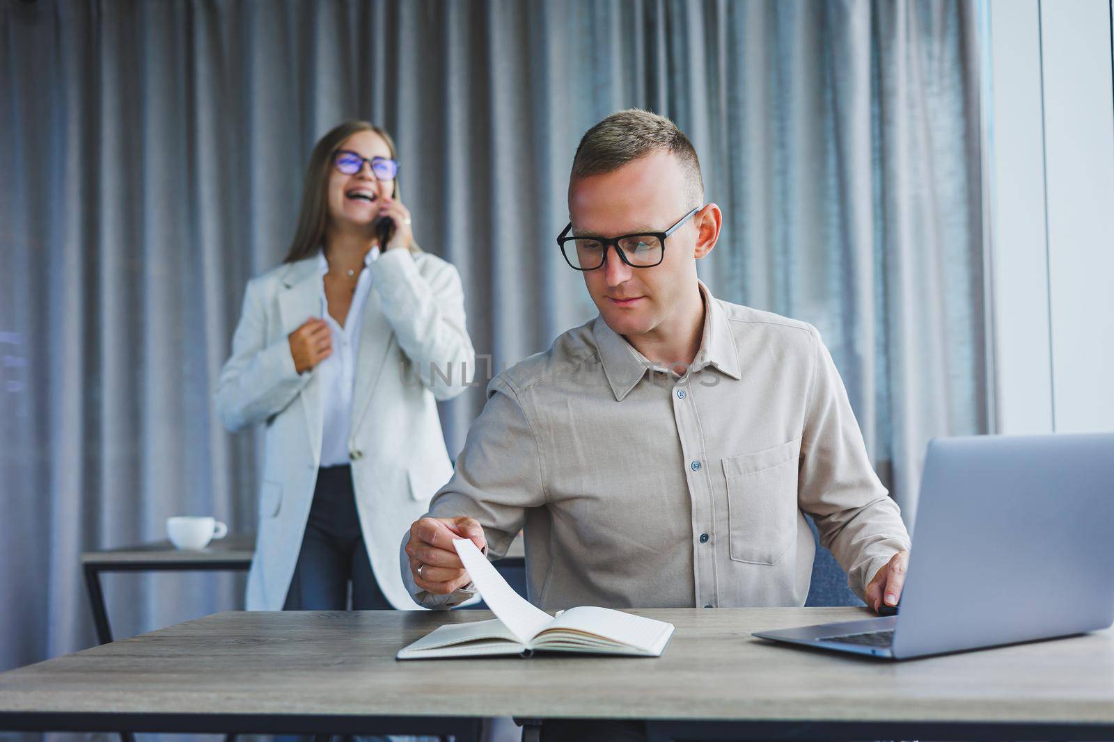 A business woman in front of a male colleague who works at a laptop. Business cooperation and teamwork. European office workers at the table in the office. Modern successful people