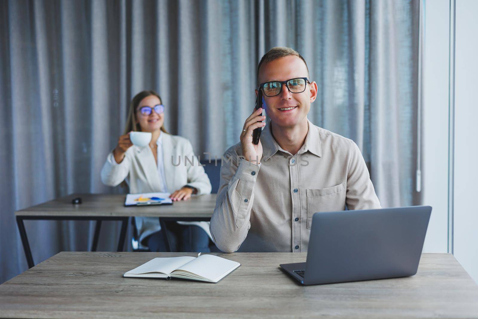 Portrait of a cheerful man, IT professional, working with a modern laptop, sitting at a table and smiling at the camera during a break, a happy human programmer in vision correction glasses