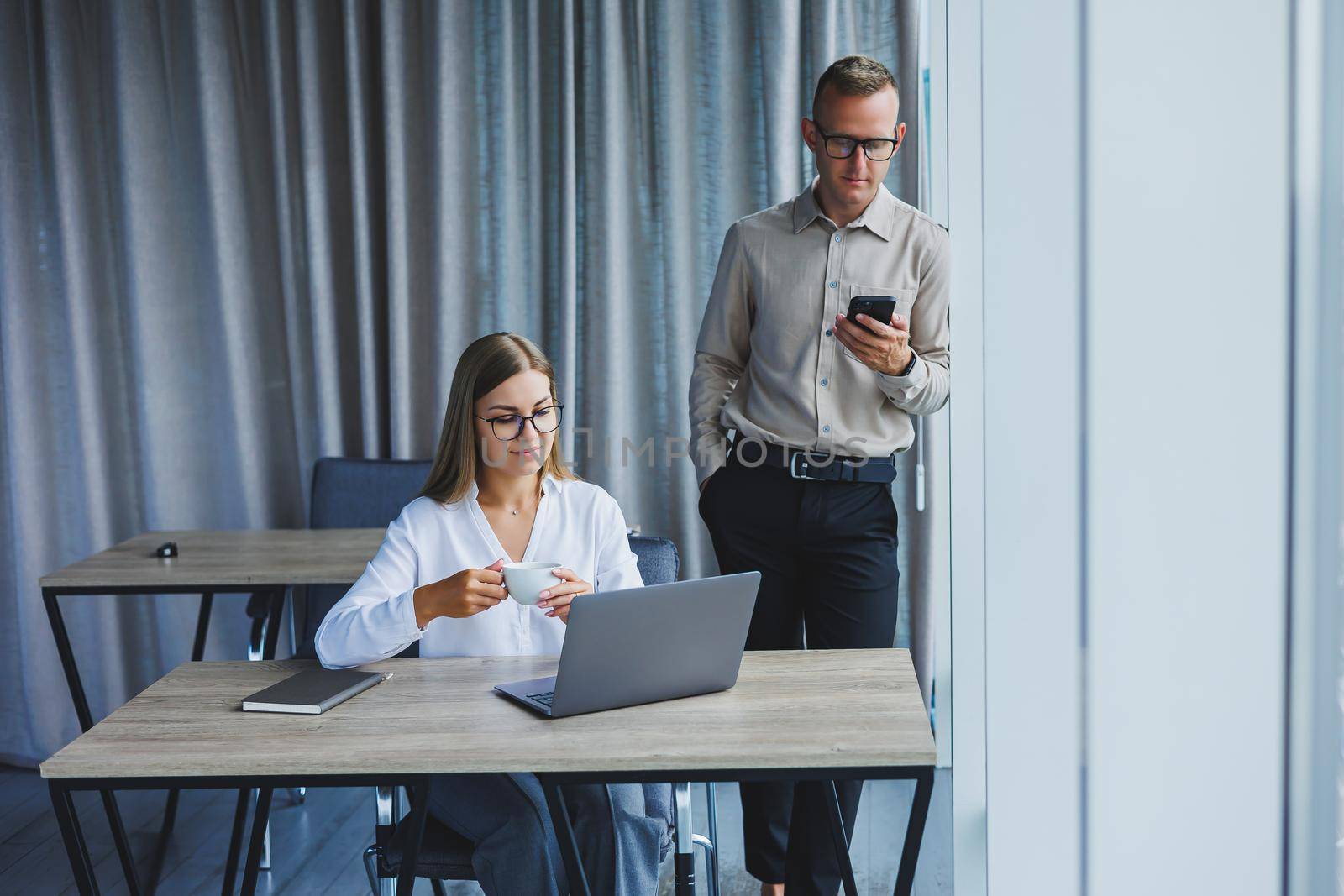 Confident male and female colleagues in elegant casual wear are discussing a project in the workplace, enjoying corporate friendship, happy partners are talking about office networks on a mobile phone