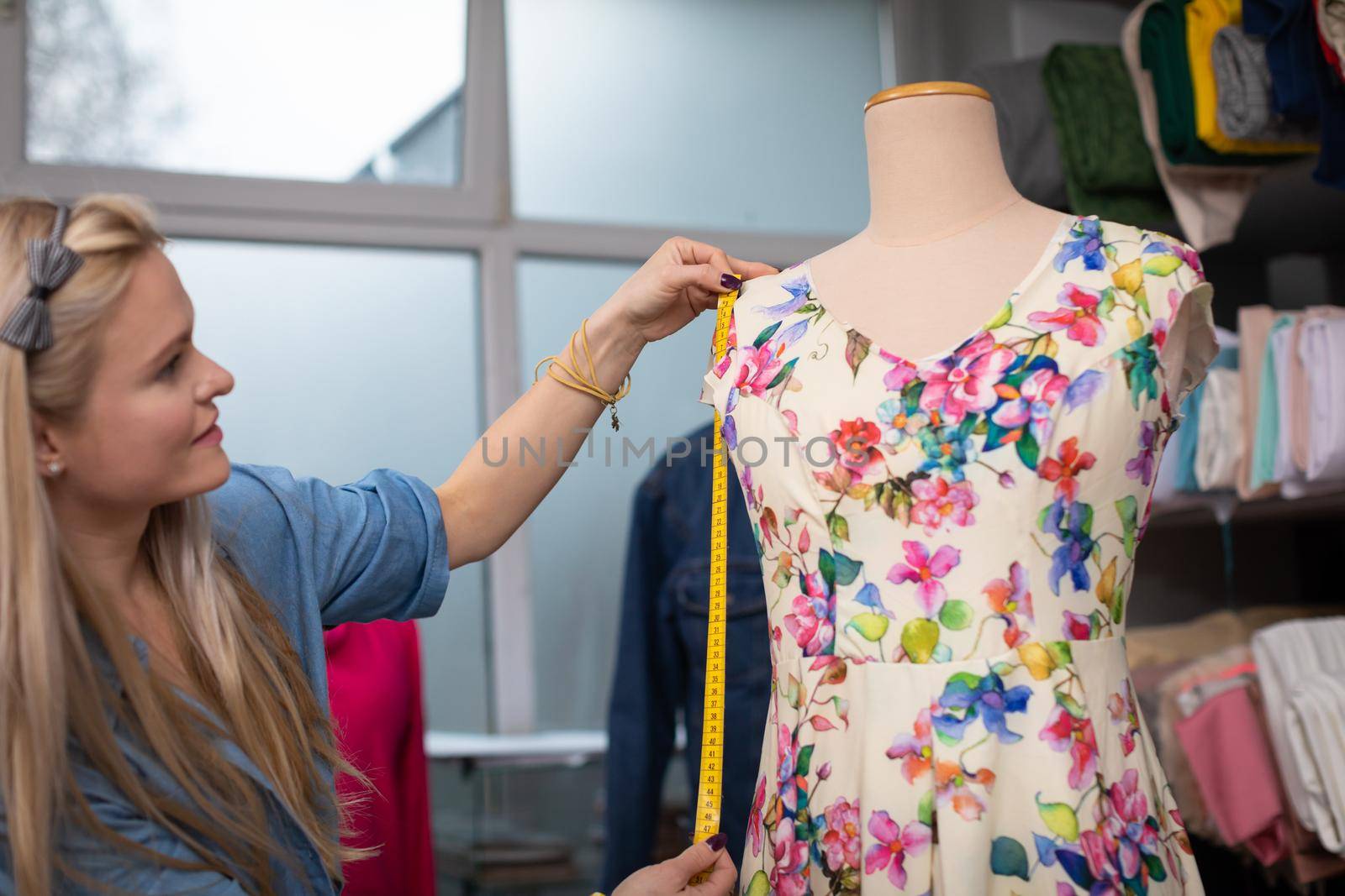 A clothing designer measures a freshly sewn dress, which is put on a mannequin. Tailor's workshop at work.