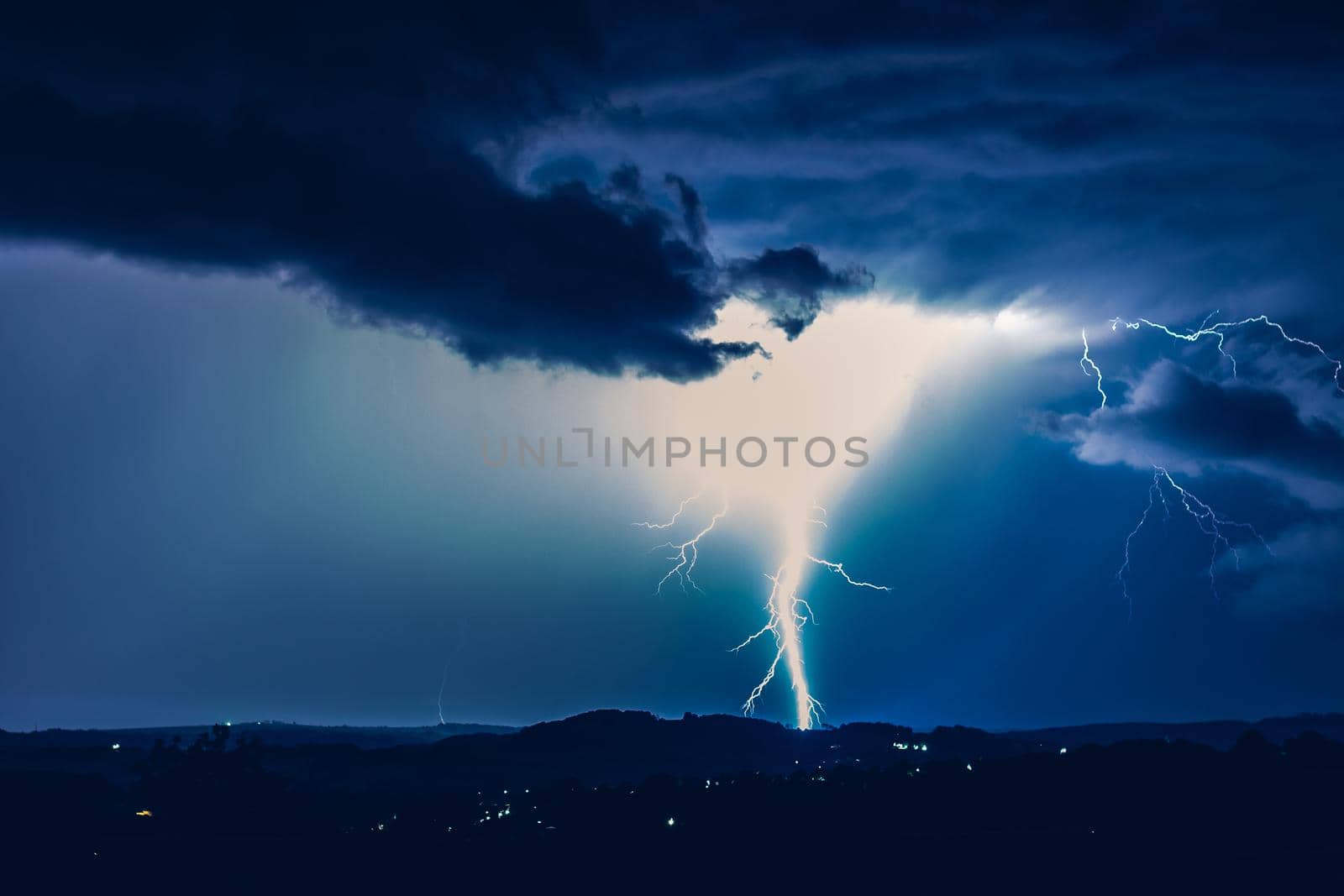 Night landscape on a background of thunderstorms. Rural silhouette and clouds with lightning flashes