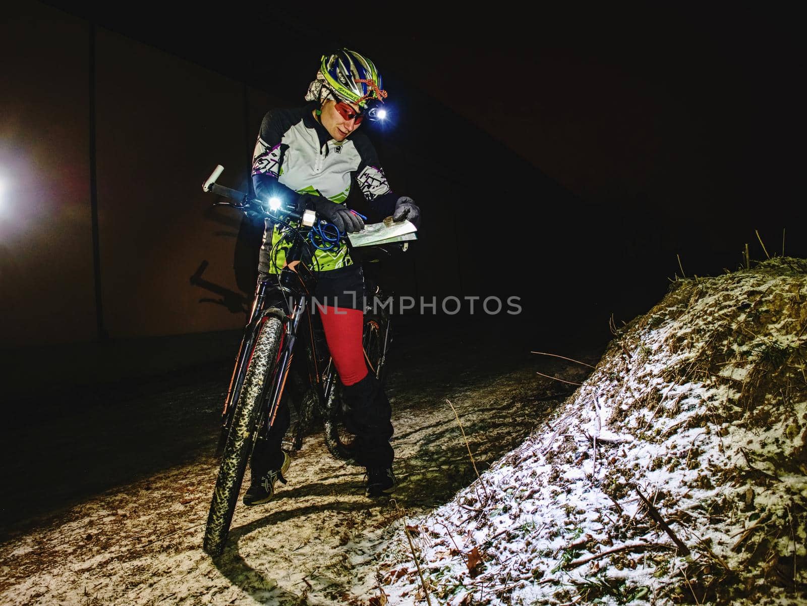 Outdoor orienteering extreme bike race in night. January 25th 2019, Novy Bor, Czech Republic. Woman check the map. Kind of sports that require navigational skills using a map and compass to achieve target.