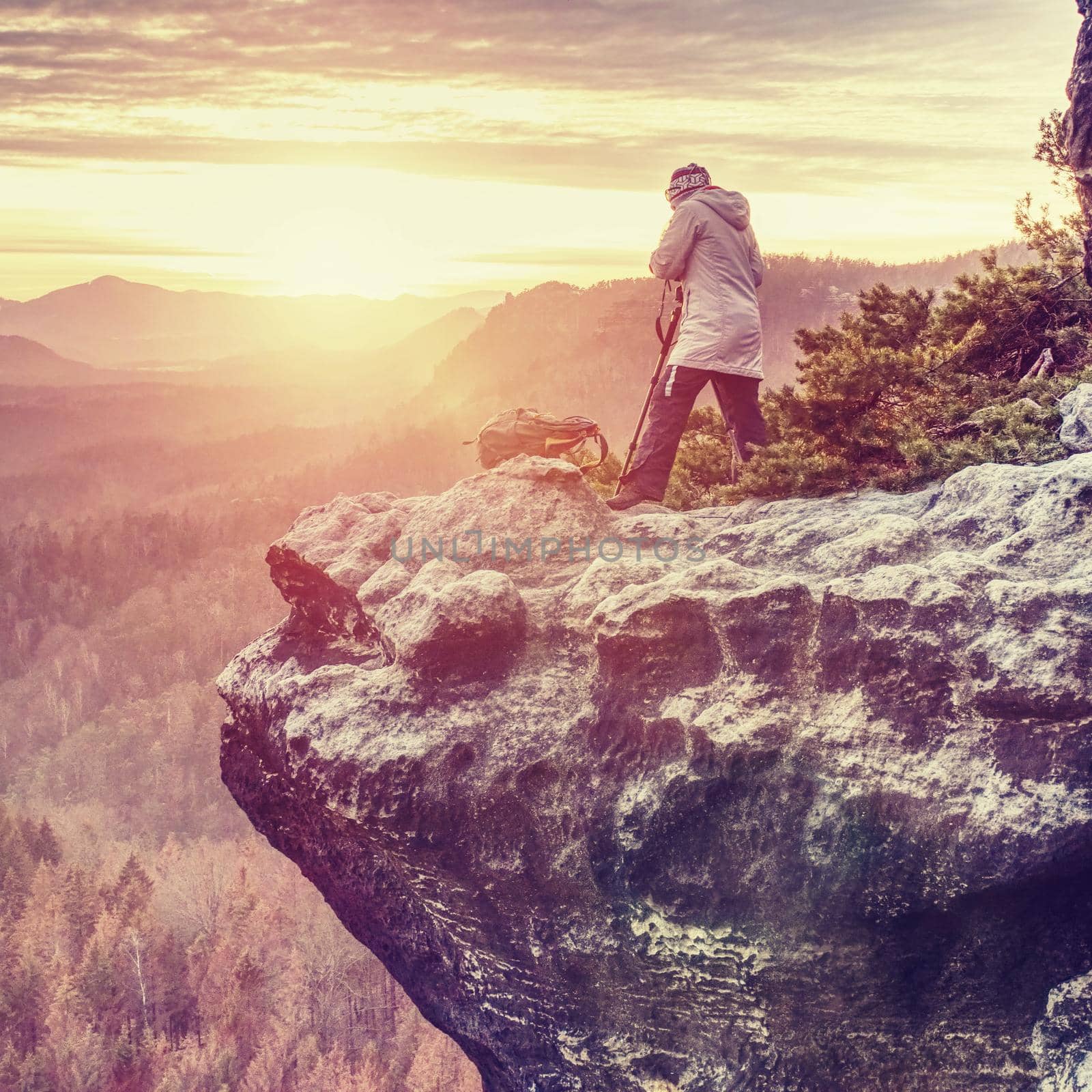 Woman hiker and photographer set tripod with camera on exposed rock above deep misty valley