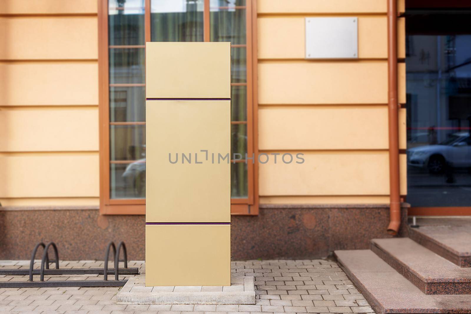 Close-up, a large sign in front of the hotel entrance to indicate the entrance, parking and other information, mockup. City, gold metal sign against the background of a yellow building on a sunny day