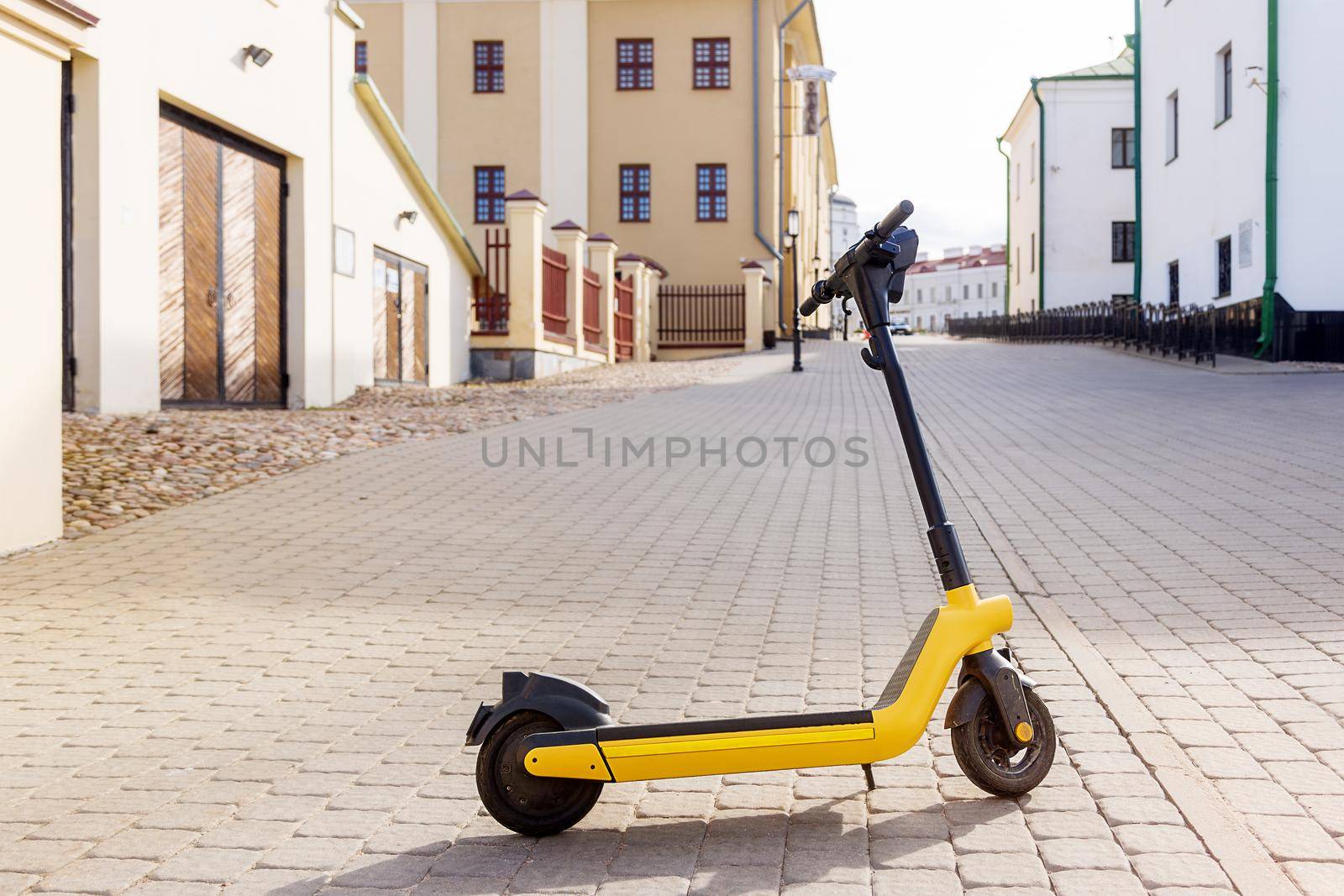 Yellow e-scooter in the old town on a summer day, per minute rent, copy space by Ramanouskaya
