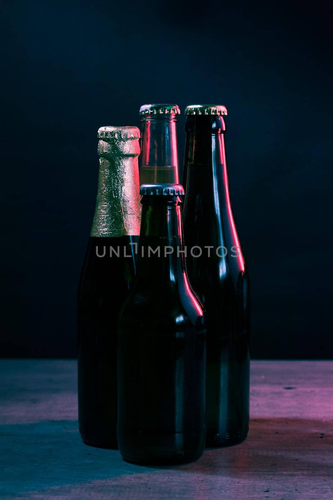silhouettes of four beer bottles on a black background with blue and pink lights that illuminate them from one side.