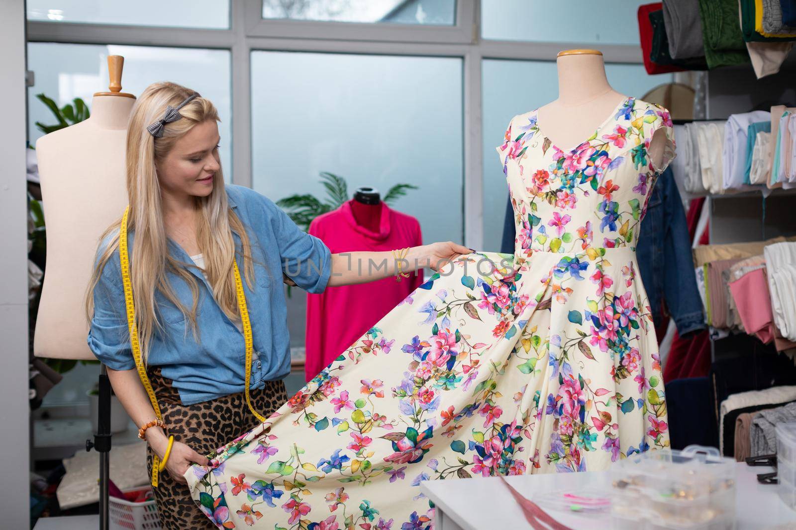 A seamstress checks a finished dress with a floral pattern. by fotodrobik