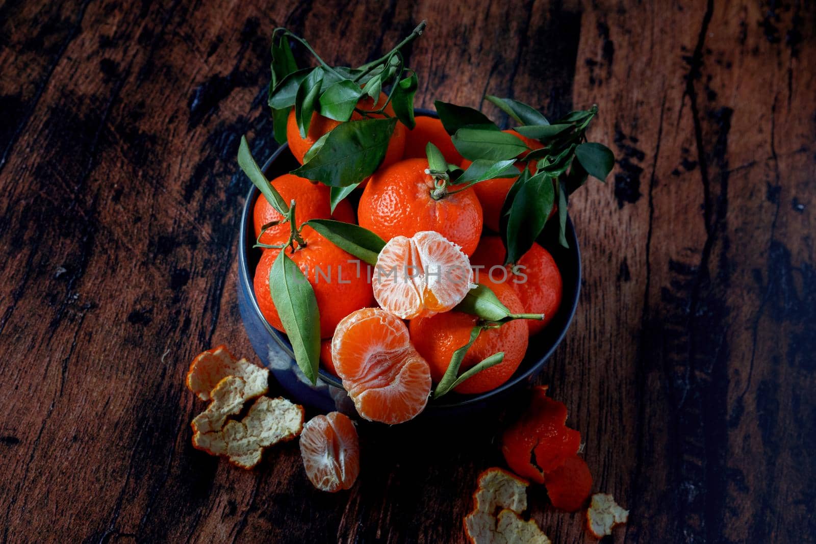 Clementines with leaves in a blue ceramic dish on an old wooden table