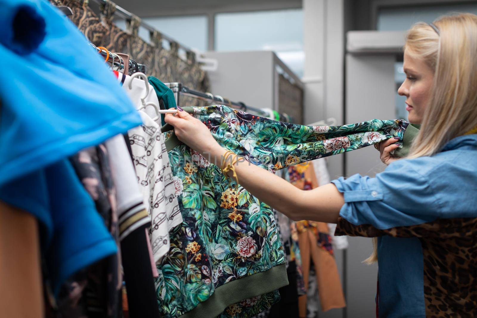 A woman looks at the new clothes hanging on the hangers. A blonde woman with long hair looks for the right blouse for her.