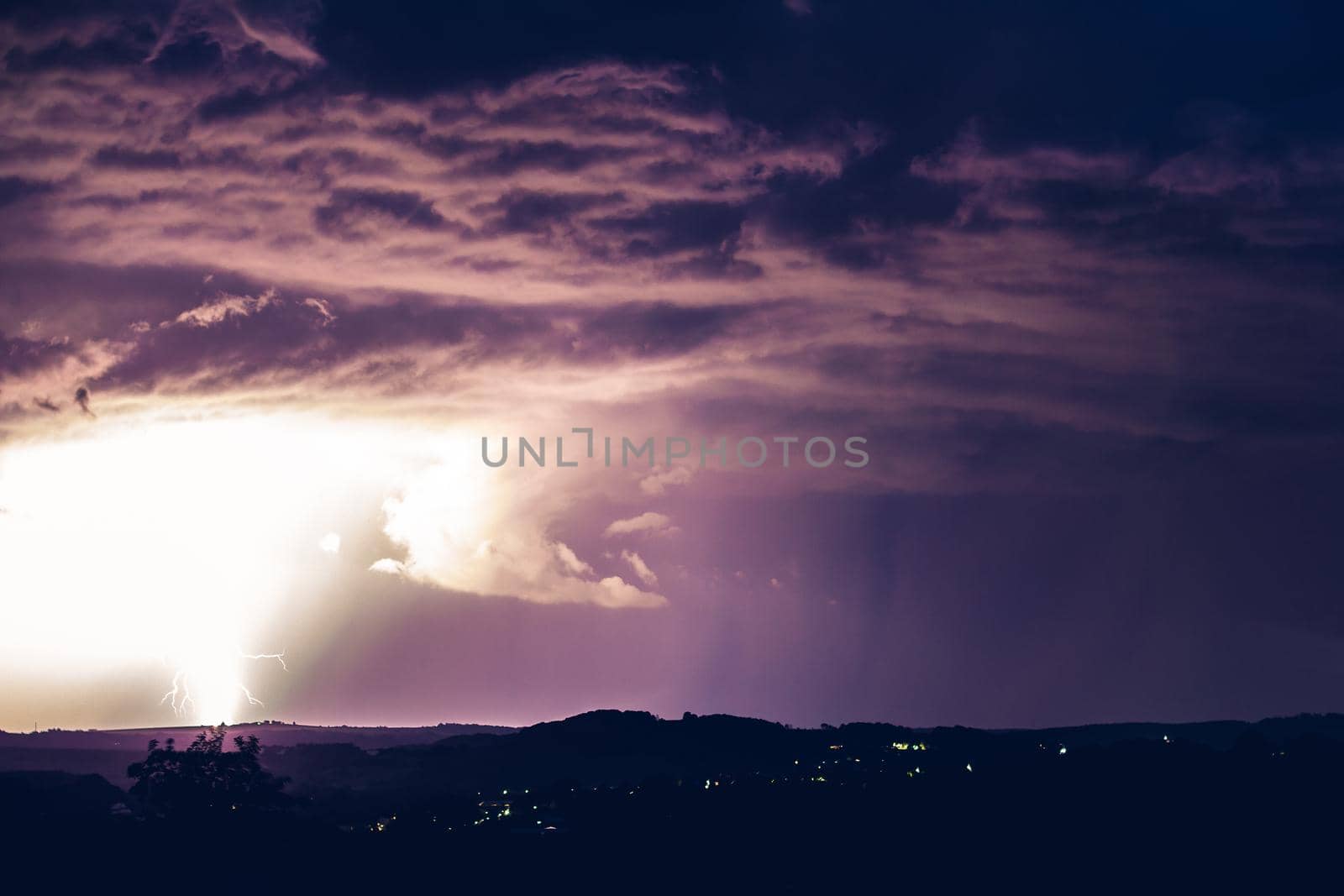 Night landscape on a background of thunderstorms. Rural silhouette and clouds with lightning flashes