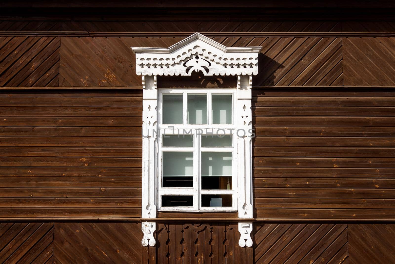 carved window in Russian old style with white architraves, on wooden background by Ramanouskaya