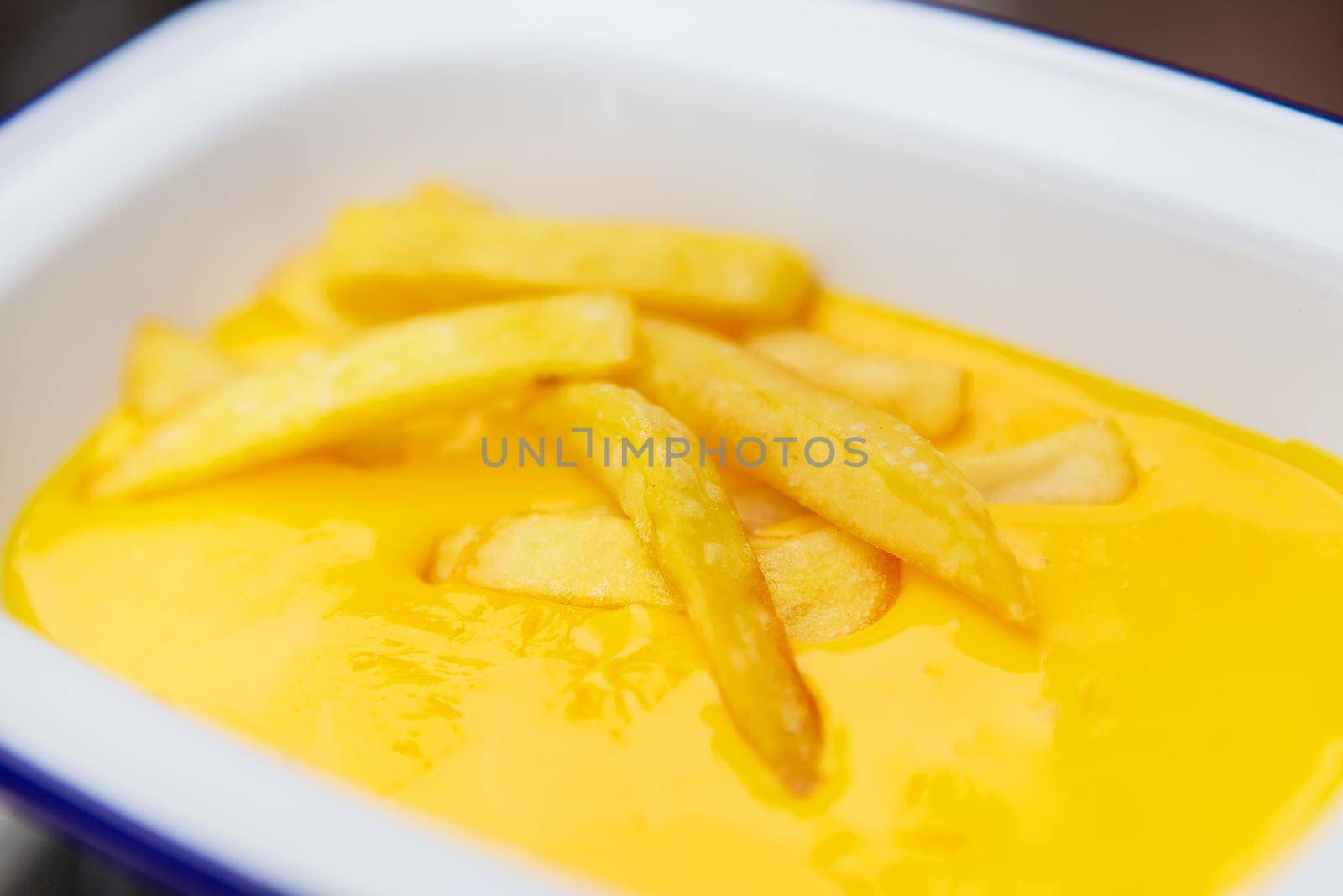 The concept of fast food and fast food. French fries sit in a plate along with cheddar cheese sauce. Top view, close-up