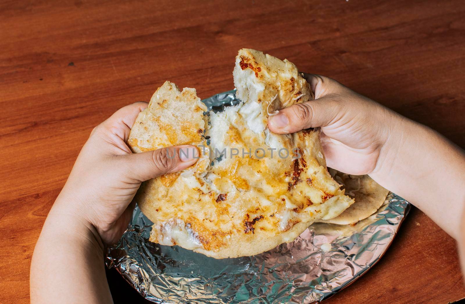 Hands dividing delicious Nicaraguan pupusa on the table, View of hands dividing delicious Salvadoran pupusas on wooden table. Concept of traditional handmade pupusas by isaiphoto