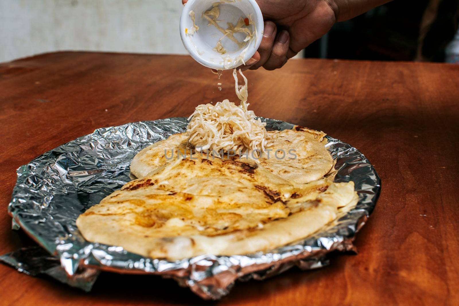 Traditional pupusas served with salad on the table. Nicaraguan pupusas with salad on aluminum foil, View of delicious Salvadoran pupusas served on wooden table. by isaiphoto