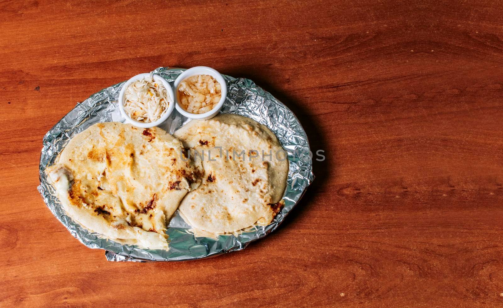 Traditional pupusas served with salad on the table. Top view of two Nicaraguan pupusas served with salad on the table. Delicious Salvadoran pupusas with melted cheese on wooden table by isaiphoto