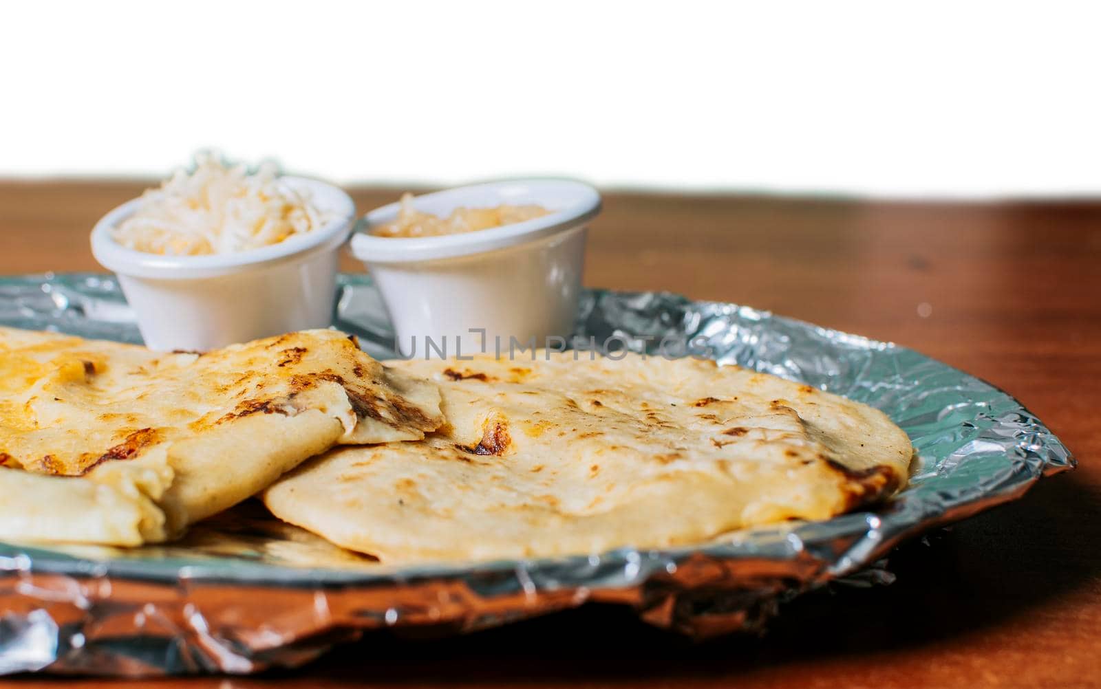 Two traditional pupusas served with salad on the table. Two Nicaraguan pupusas with salad isolated, Side view of delicious Salvadoran pupusas with cheese served on the table. by isaiphoto