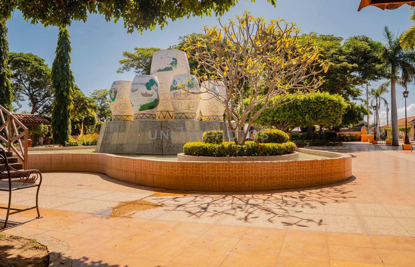 Image of a nice and relaxed park with a water fountain surrounded by trees, Traditional park of Nagarote, Nicaragua. View of a calm park with a small wooden bridge on a sunny day. Nagarote central park