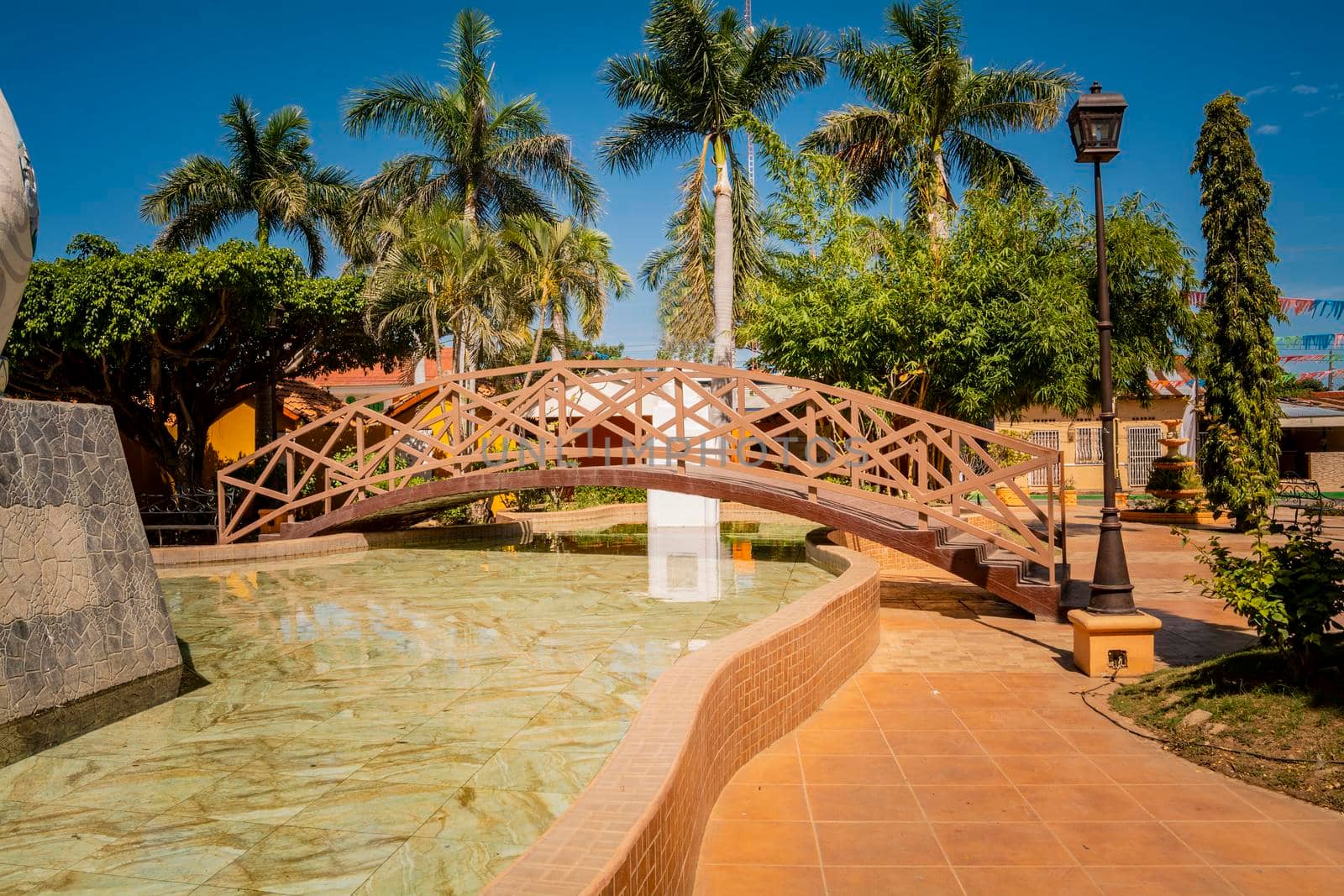 Side view of a small wooden bridge over a water fountain in a calm park. Nagarote central park.  View of a nice and relaxed park with a water fountain. Traditional park of Nagarote, Nicaragua